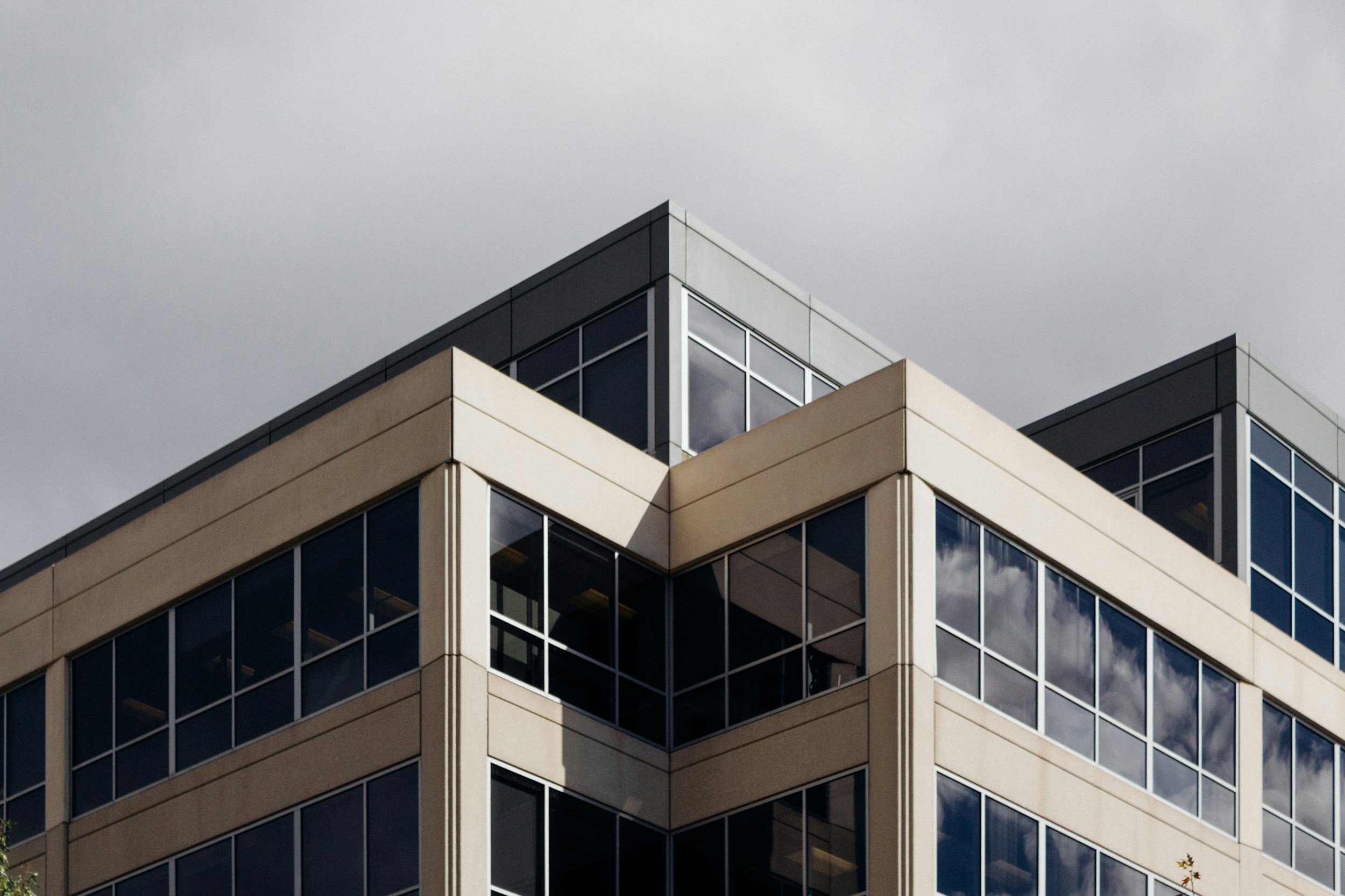 Close-up of a modern multi-story building with glass windows and beige and black exterior panels, under a cloudy sky.