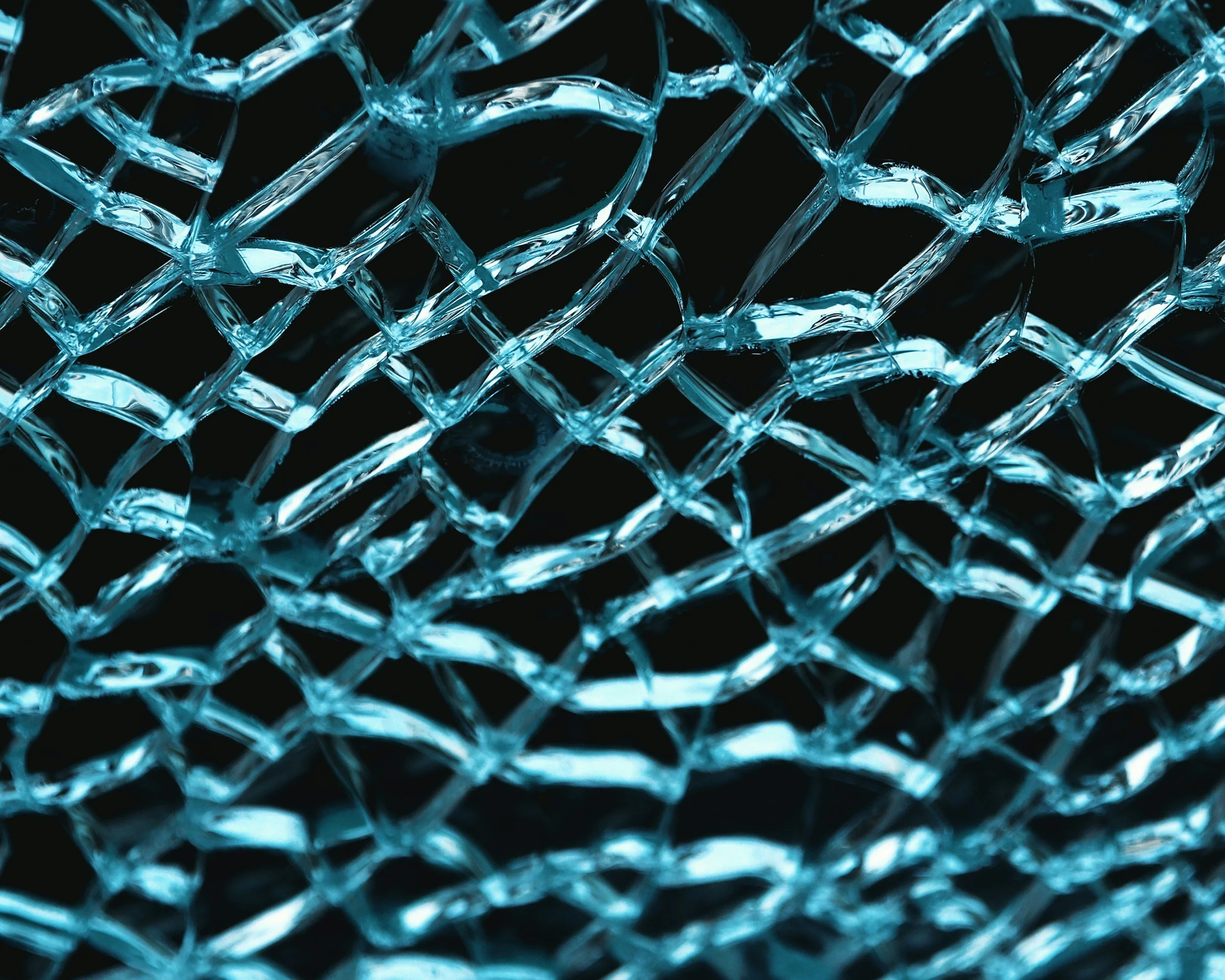 Close-up of interwoven glass or crystal strands with a blue tint, creating a textured, reflective surface against a black background.