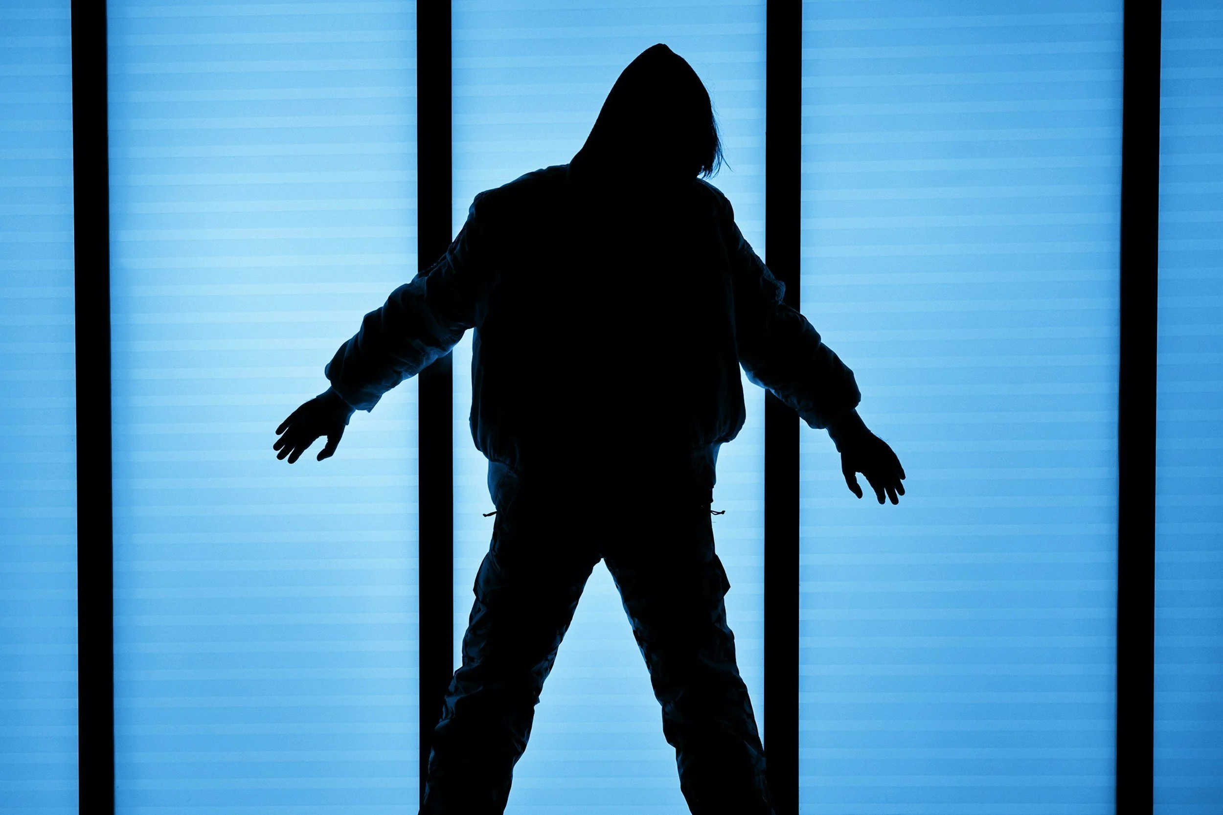 Silhouette of a person standing in front of a backlit blue background with vertical black bars.