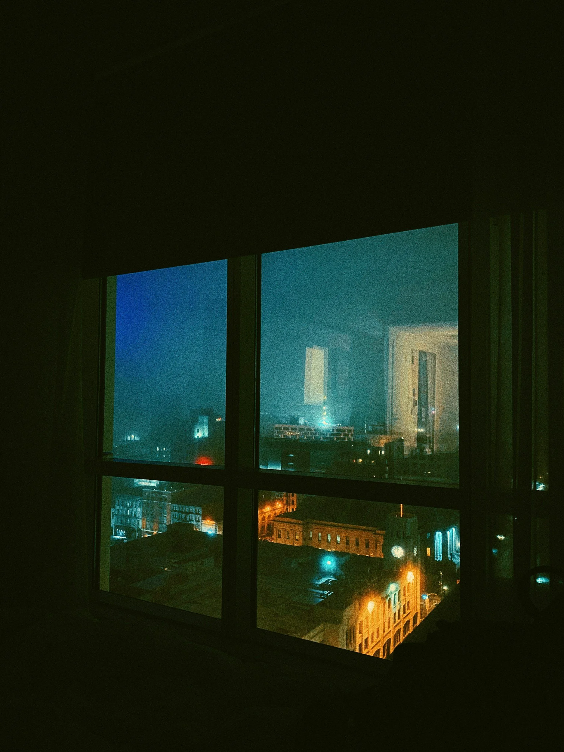 Nighttime city view through a window showing buildings and street lights.