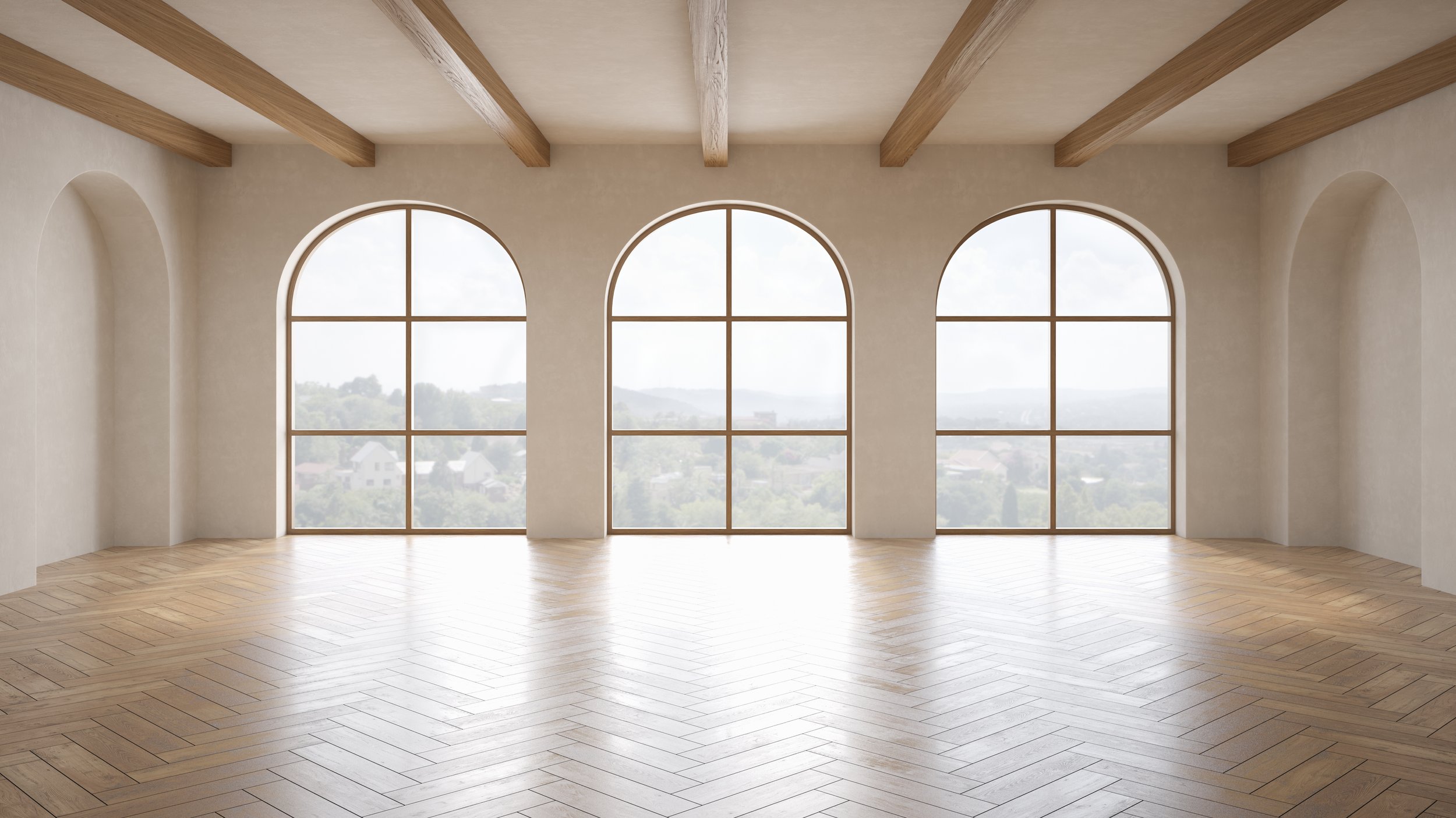 Empty room with large arched windows, beige walls, wooden ceiling beams, and light wood flooring showing a distant landscape.