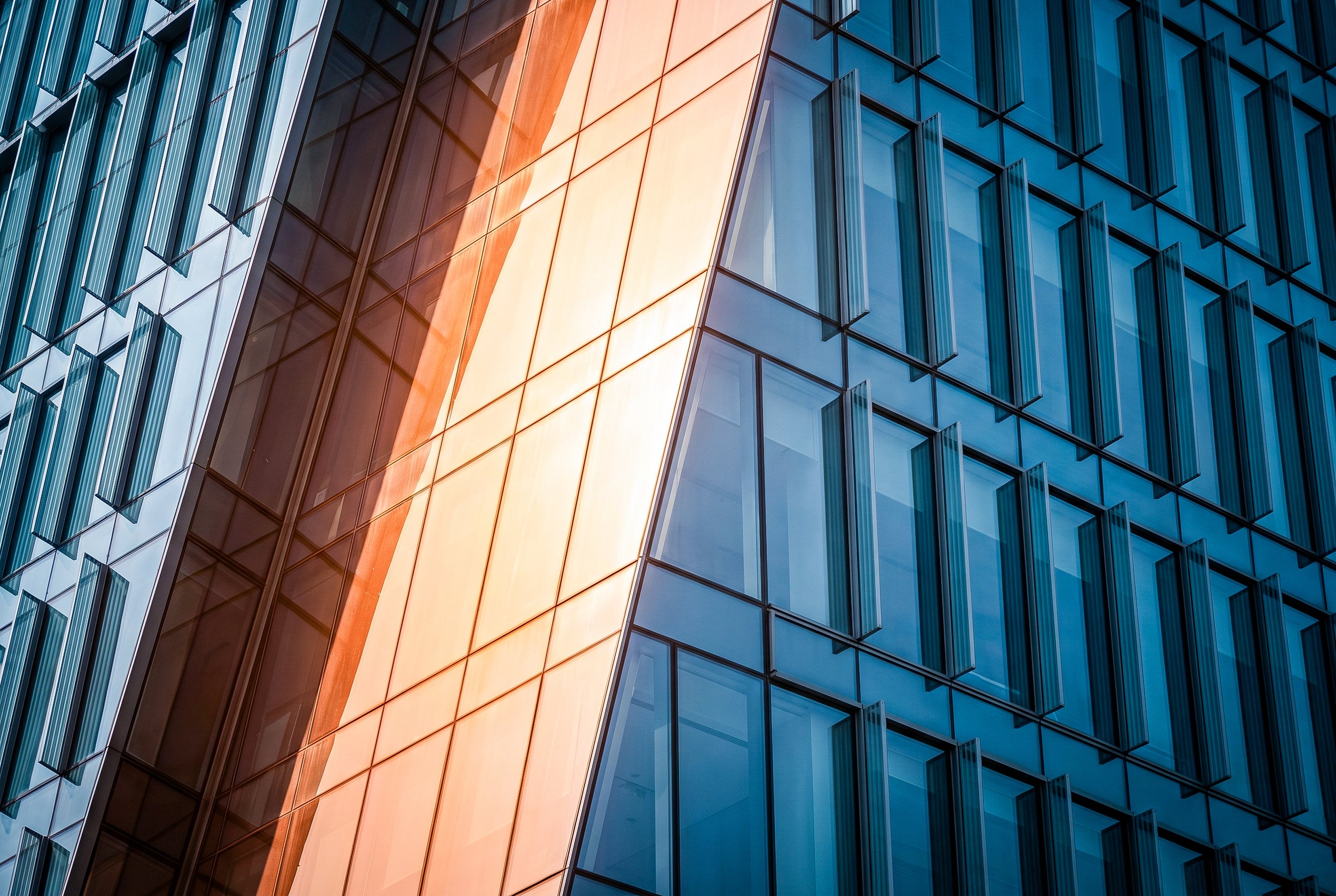 Close-up of the glass facade of a modern high-rise building, featuring reflective windows and orange-colored panels.