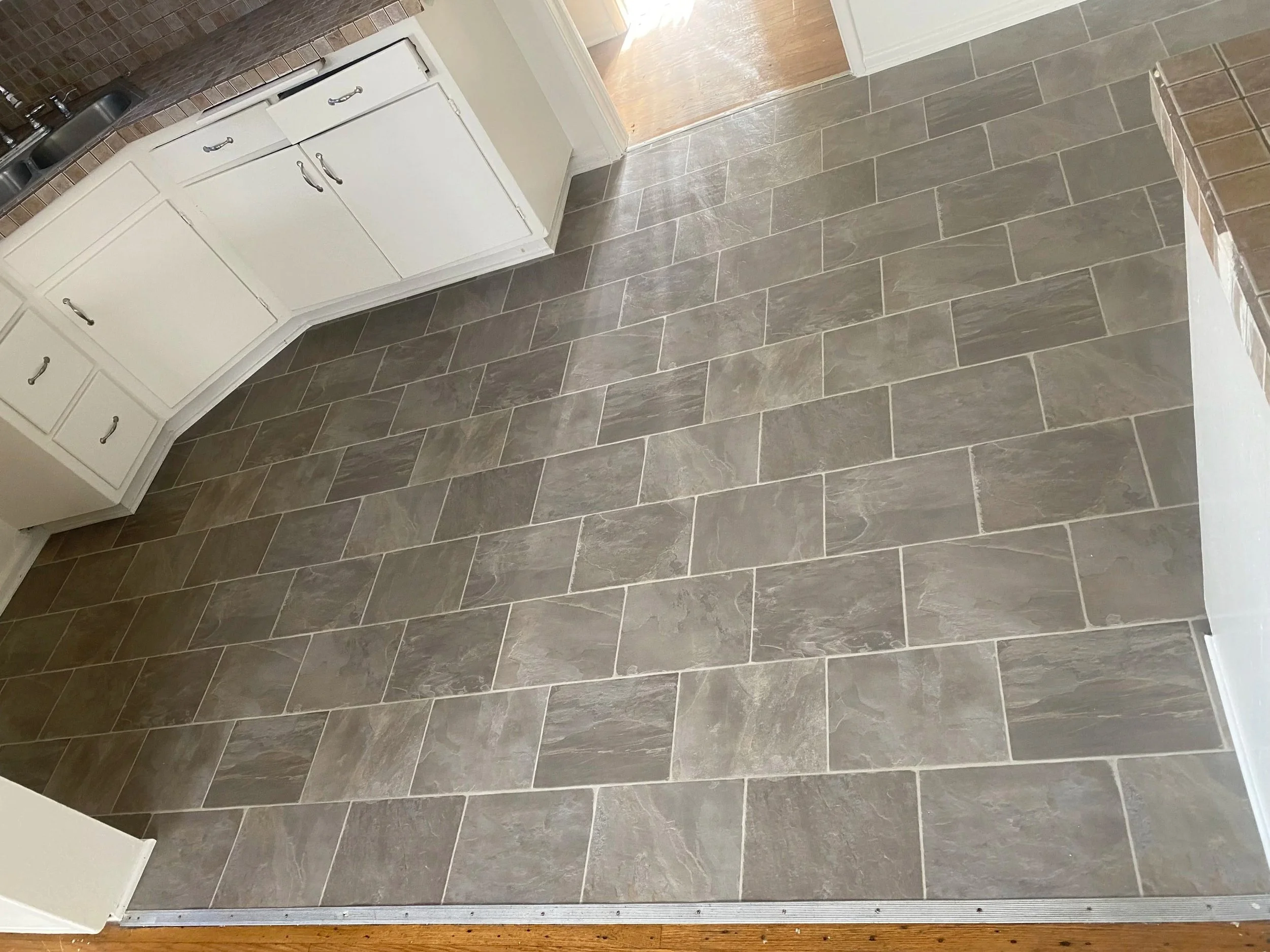 Photo of a kitchen with gray tile flooring, white cabinets, and a granite countertop with a sink.