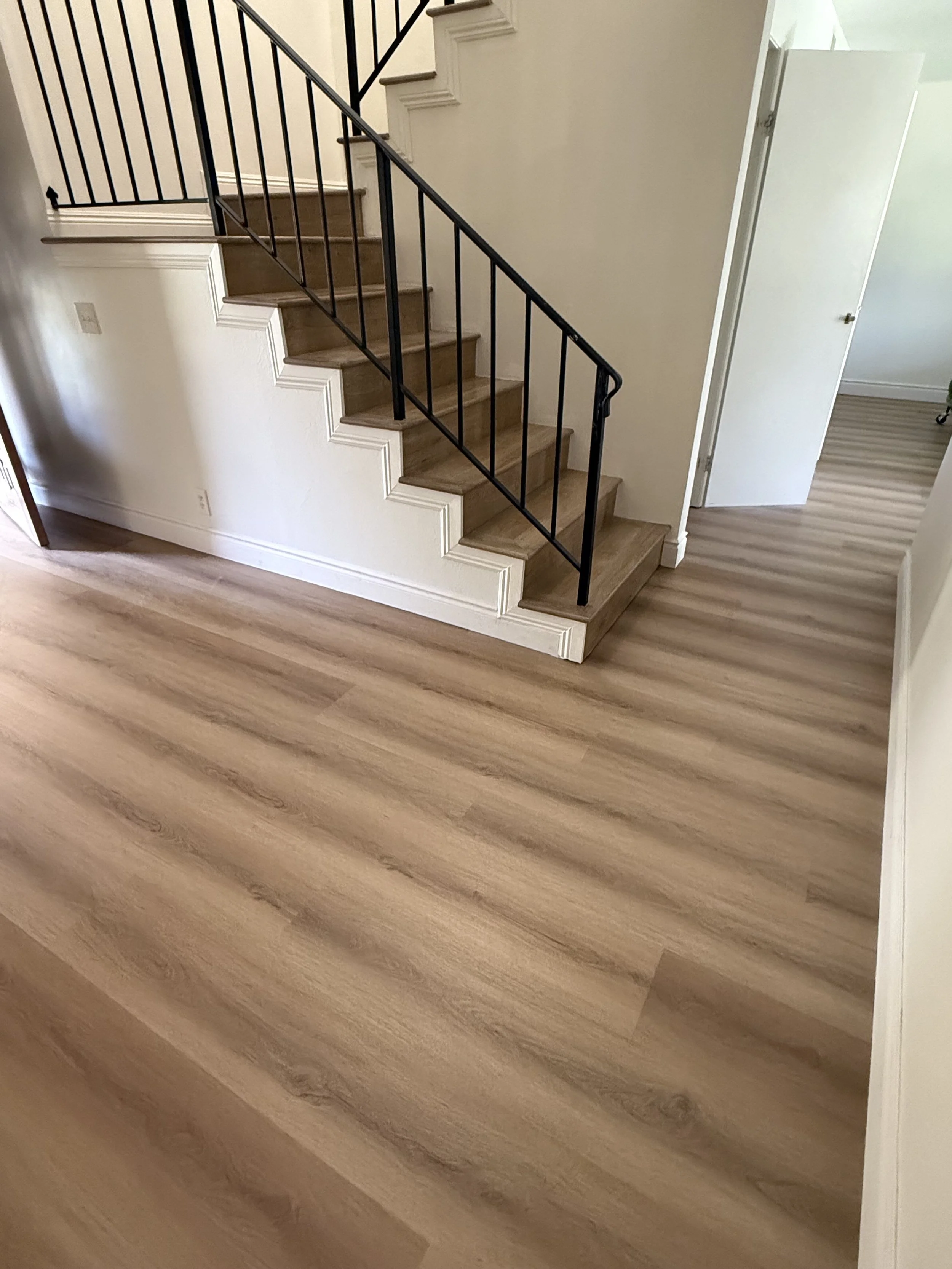 Interior view of a staircase with wooden steps, black metal railing, white walls, and laminate wood flooring.