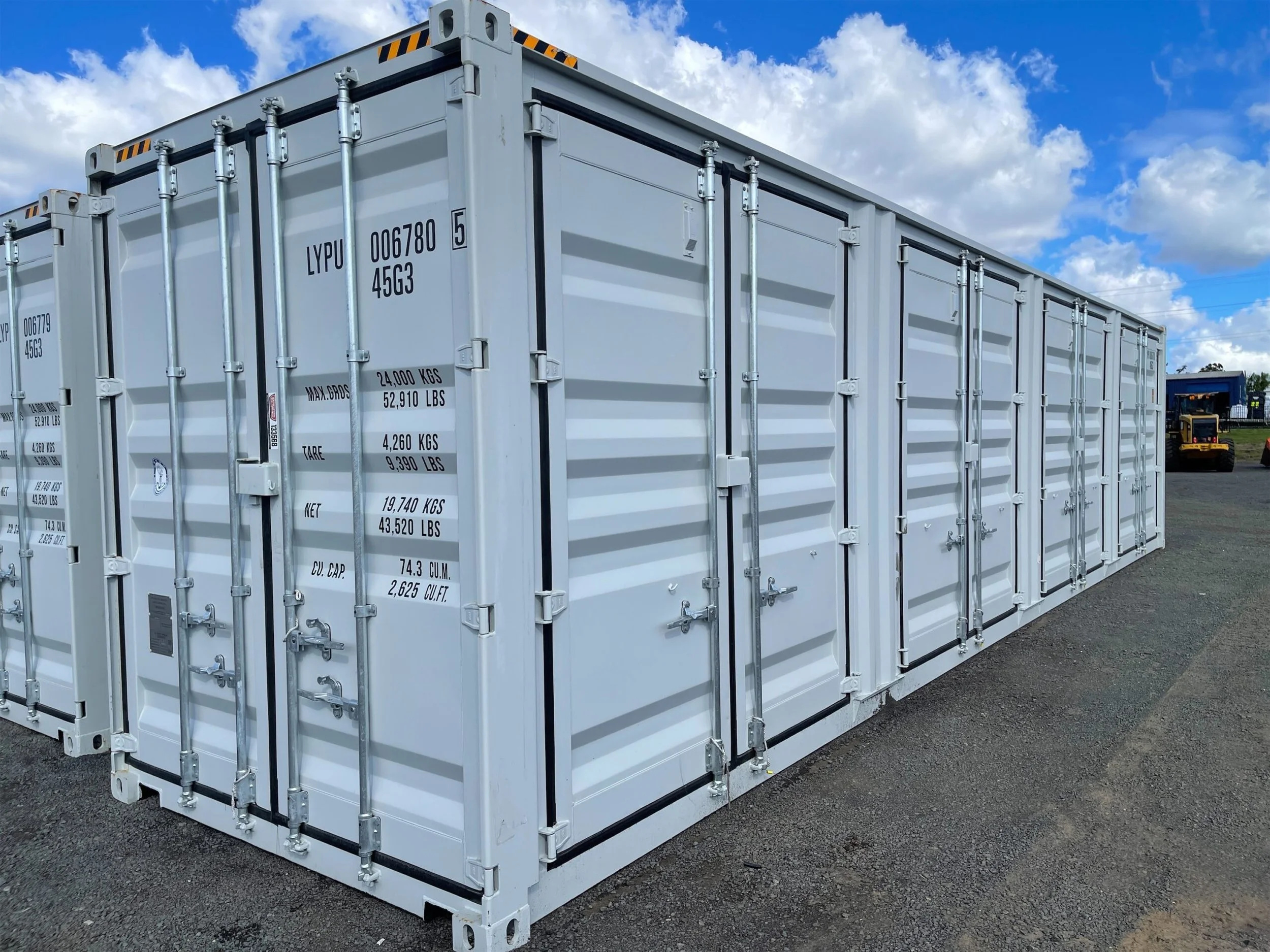 Row of white shipping containers at an outdoor storage yard under a blue, cloudy sky