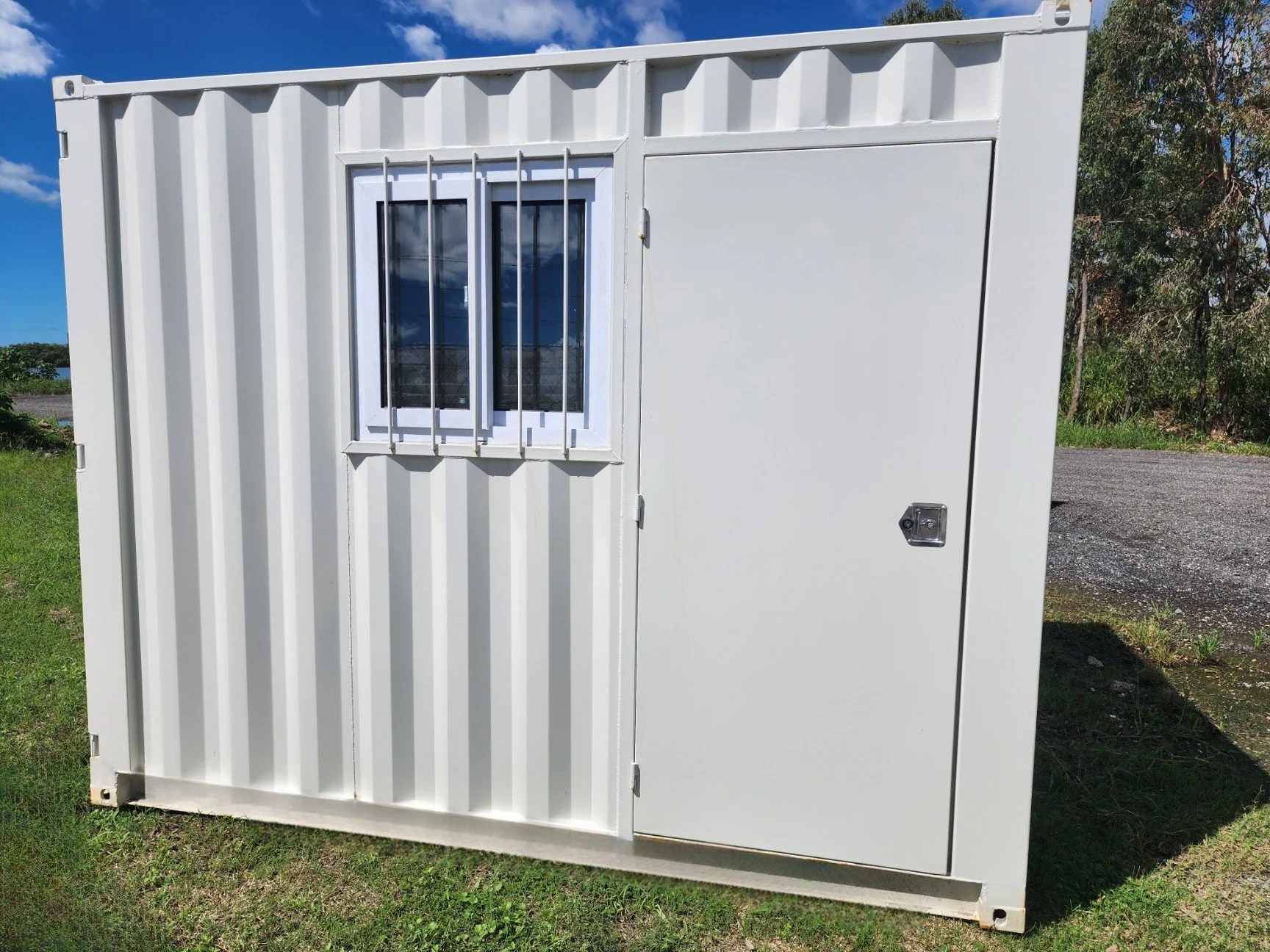 White steel shipping container with a barred window and secure door outdoors