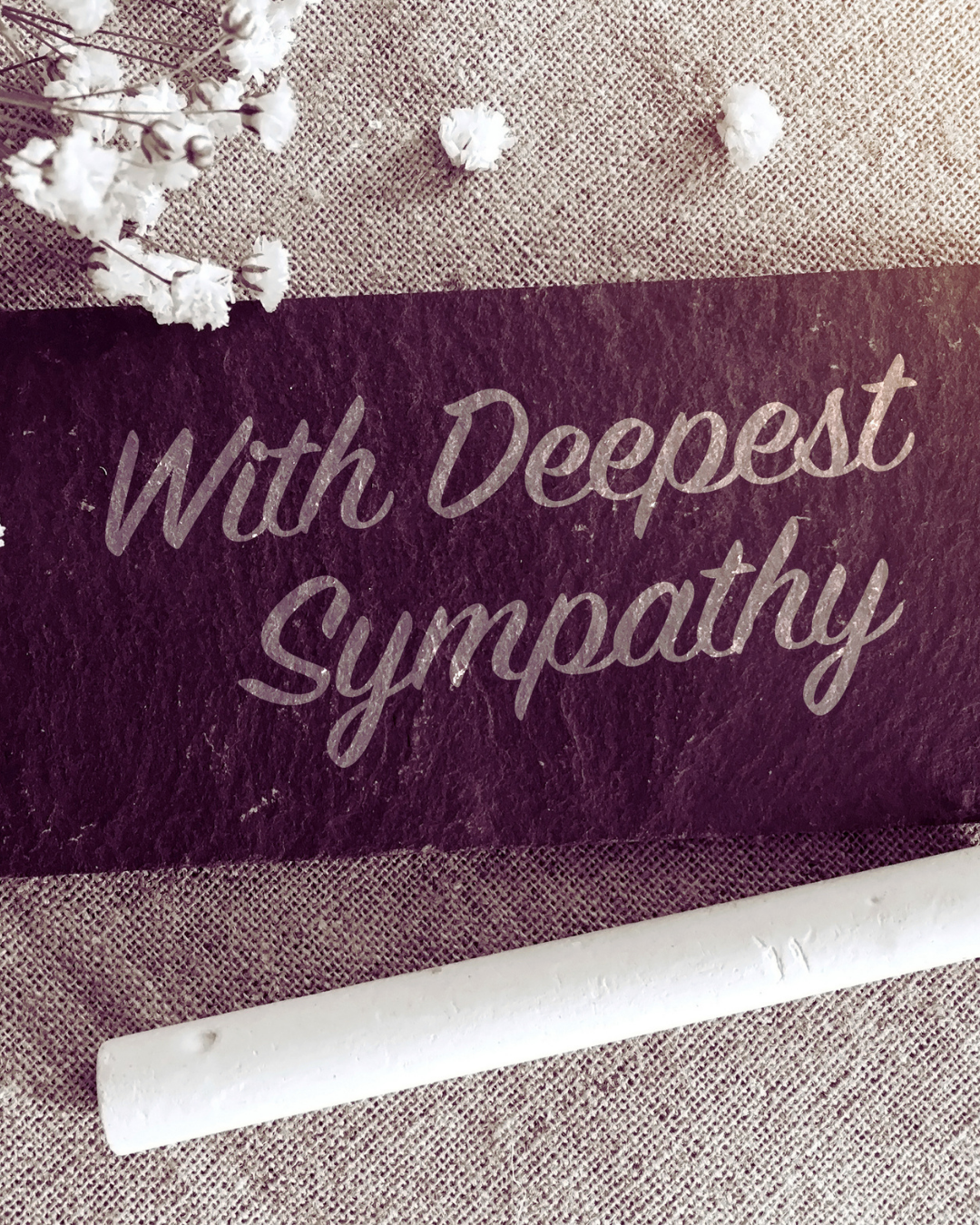 A decorative sign with the words 'With Deepest Sympathy' written on it, placed on a textured table with white flowers nearby.