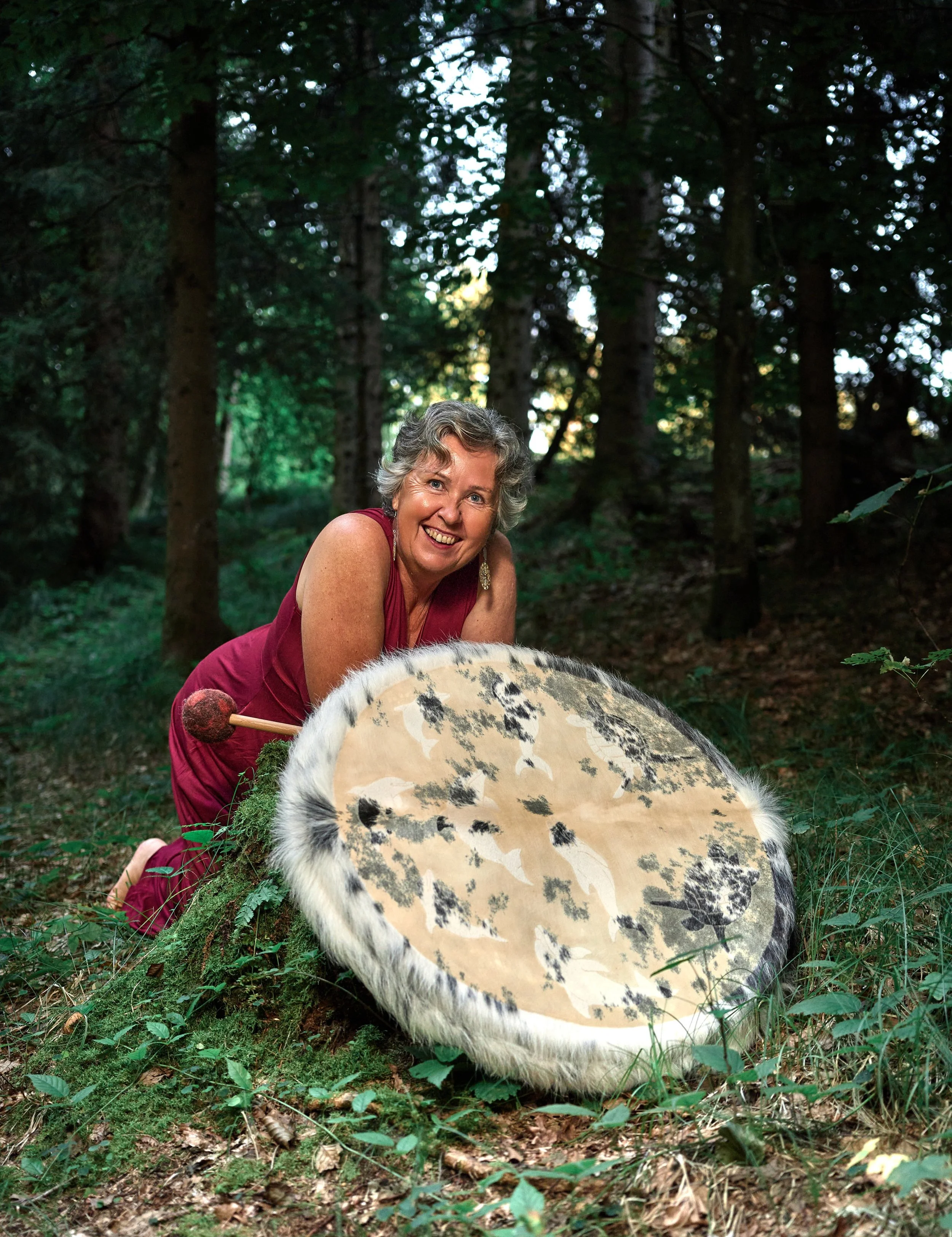 Eine lachende Frau in einem roten Kleid mit einem großen Trommel im Wald.