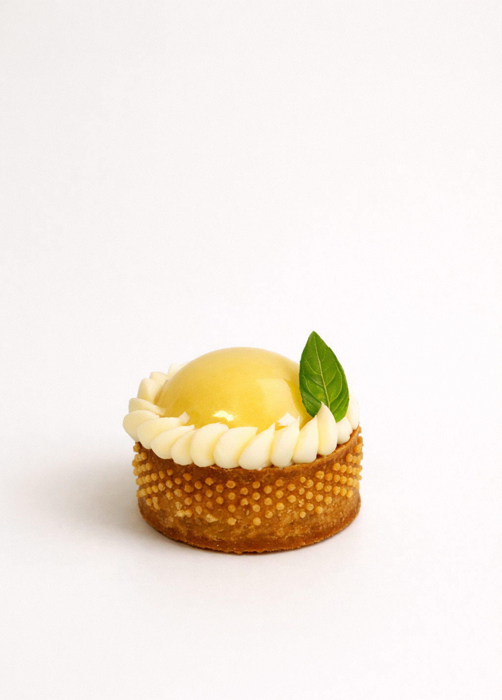 Handcrafted lemon tart petit four with a glossy golden glaze and fresh leaf garnish.