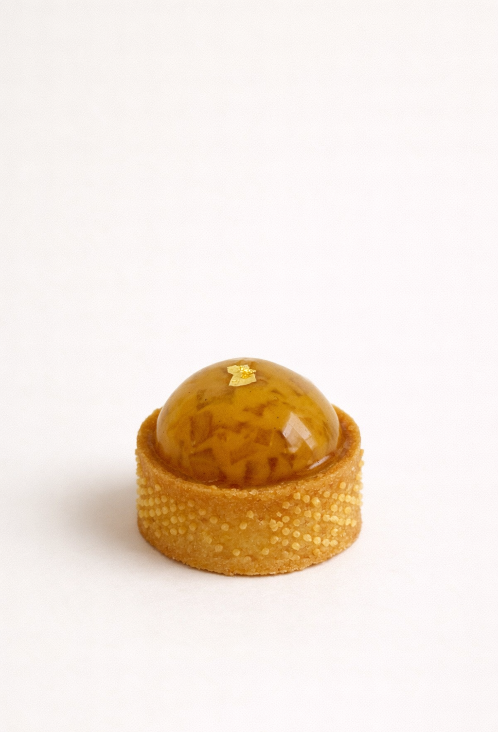 Artisan caramelised apple tart petit four with a glossy glaze and gold leaf accent.