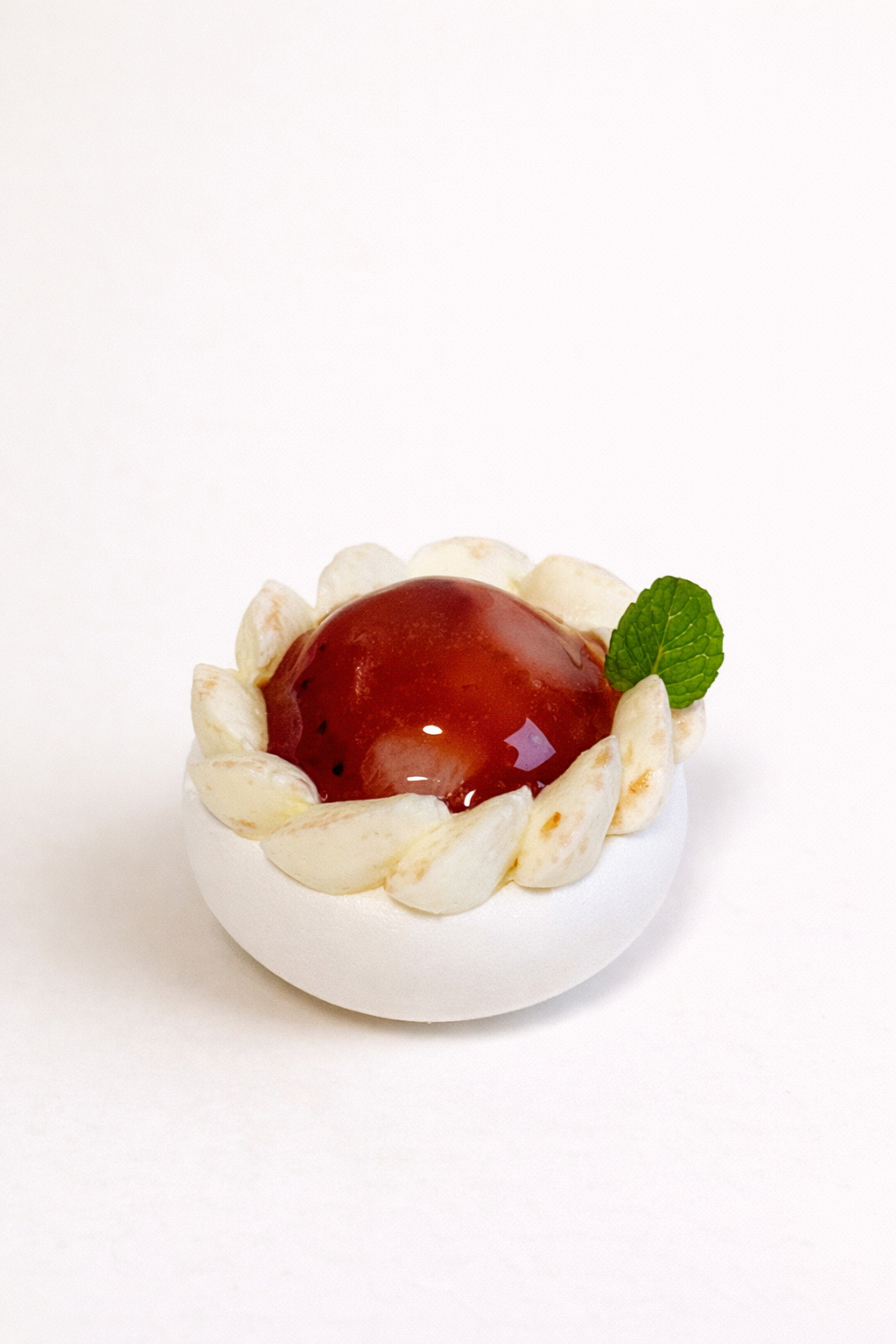 Elegant handcrafted dessert strawberry lychee pavlova petit four with a glossy red centre, piped cream, and fresh mint.
