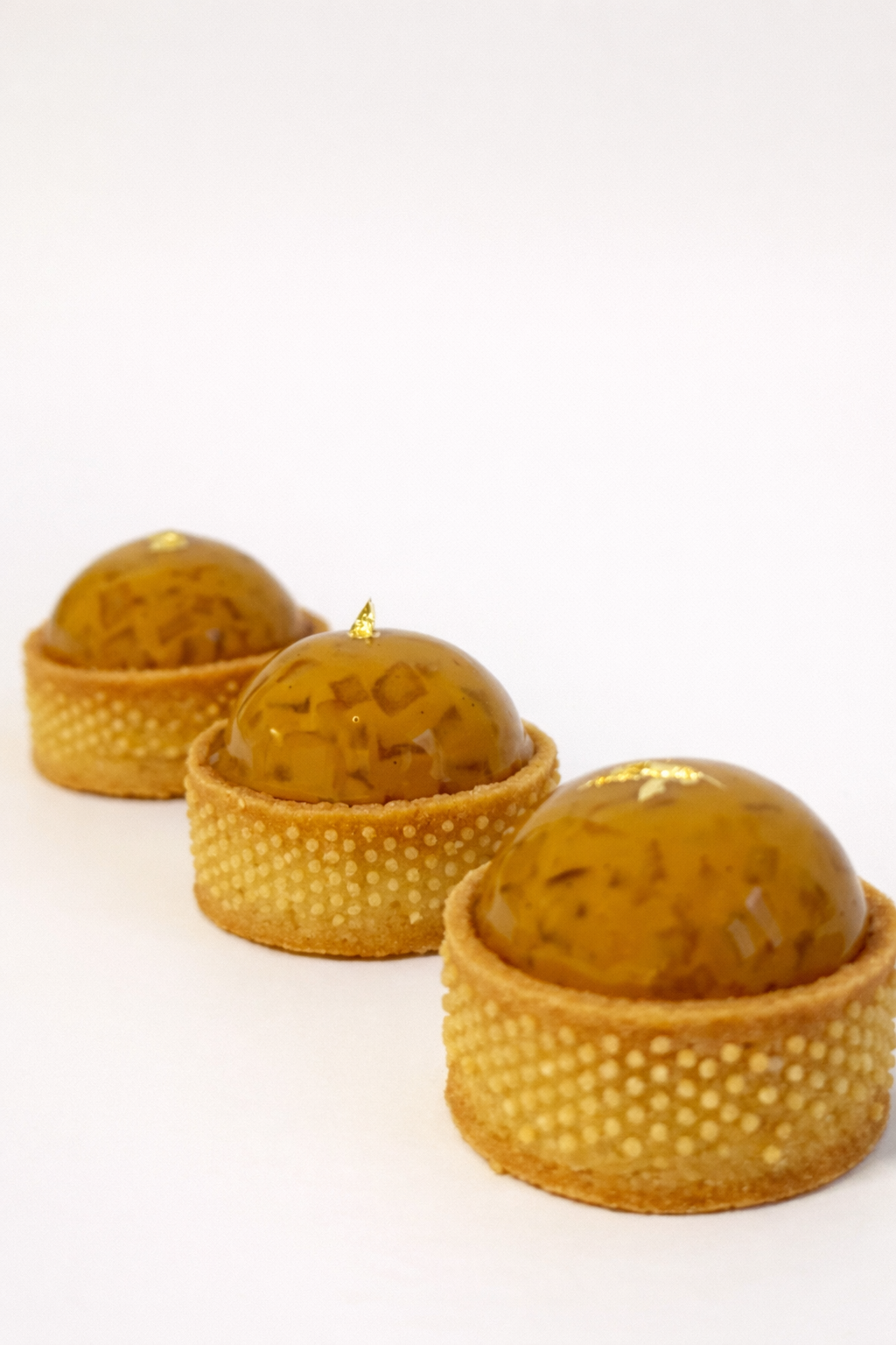 Three premium caramelised apple tarts lined up diagonally with gold leaf details. Corporate dessert catering in Sydney.