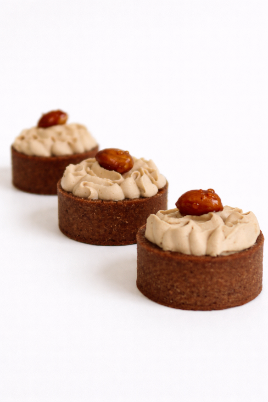 Three handcrafted peanut banoffee tarts lined up showing the cocoa shell and salt-roasted peanut. Artisan dessert delivery in Gordon.