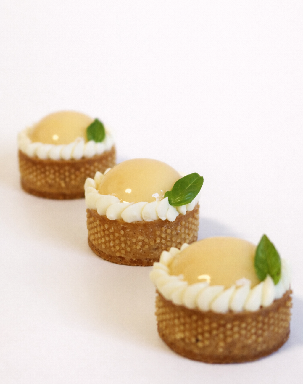 Three handcrafted lemon basil tart petit fours lined up. Artisan dessert catering for corporate events in Sydney.