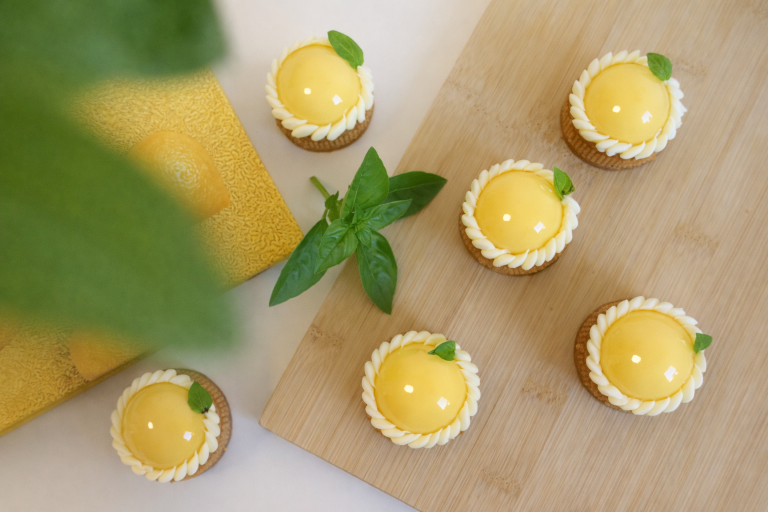 Top-down view of handmade lemon basil tarts styled on a wooden board with fresh leaves. High tea dessert catering North Shore.