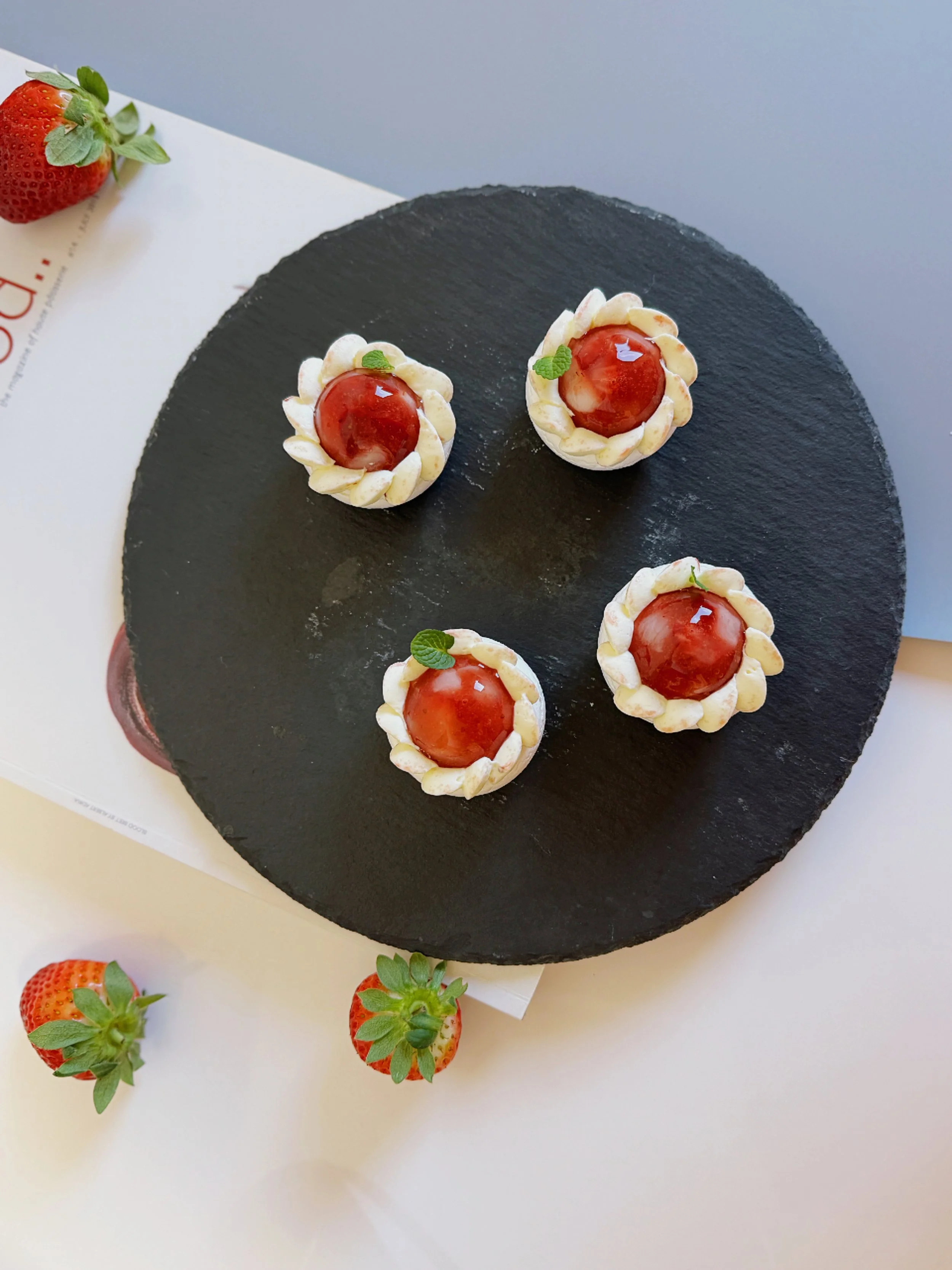 Top-down view of four strawberry lychee pavlovas served on a dark stone board. Premium high tea dessert boxes Eastern Suburbs.