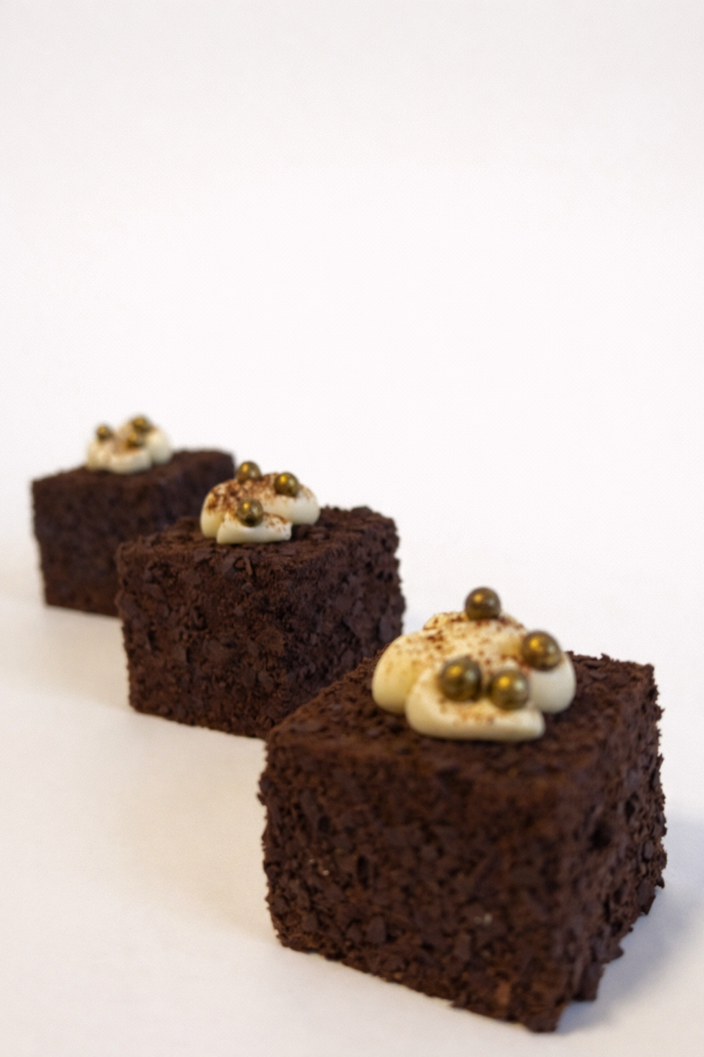 Three premium tiramisu cube petit fours lined up diagonally. Luxury corporate boardroom dessert catering Sydney.
