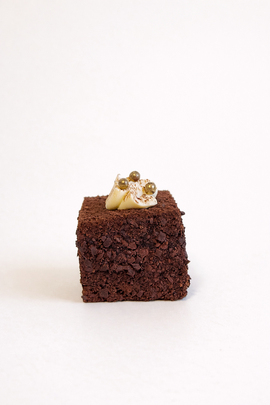 Close-up of a handcrafted tiramisu cube petit four topped with mascarpone and gold pearls. Luxury dessert delivery in Sydney.