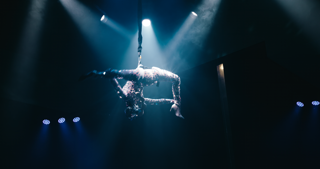 Aerial performer suspended upside down on a trapeze under stage lights
