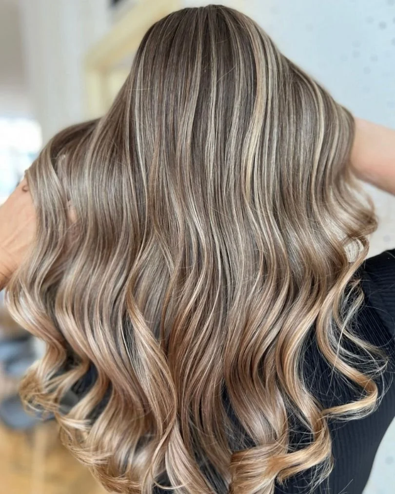 Close-up of long, wavy hair with balayage highlights/babylights in shades of blonde and light brown.