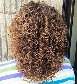 Close-up of a person's head with tight, blonde and light brown curly hair wearing a striped shirt.