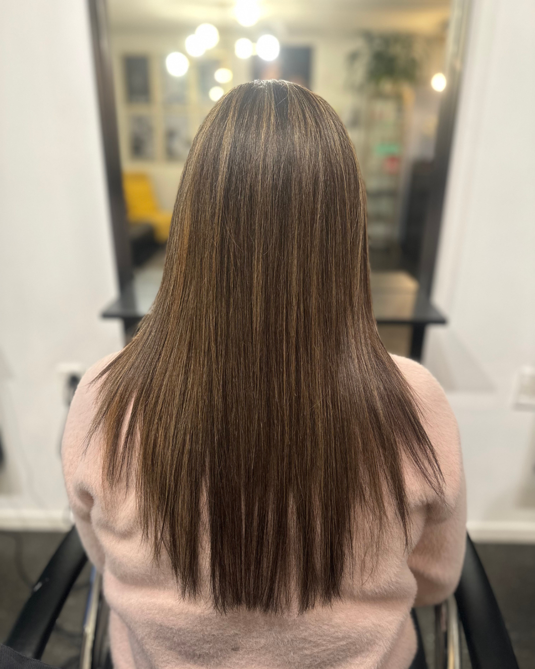 Back view of a woman with straight, shoulder-length brown hair in a salon.