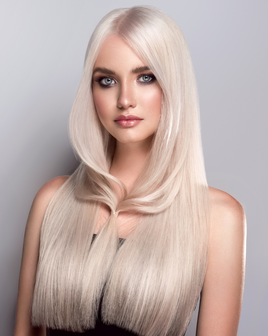 A woman with long, straight, platinum blonde hair and blue eyes posing against a light gray background.