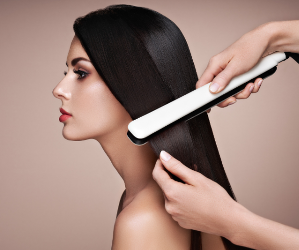 A woman with long, straight, dark hair getting her hair straightened with a flat iron.