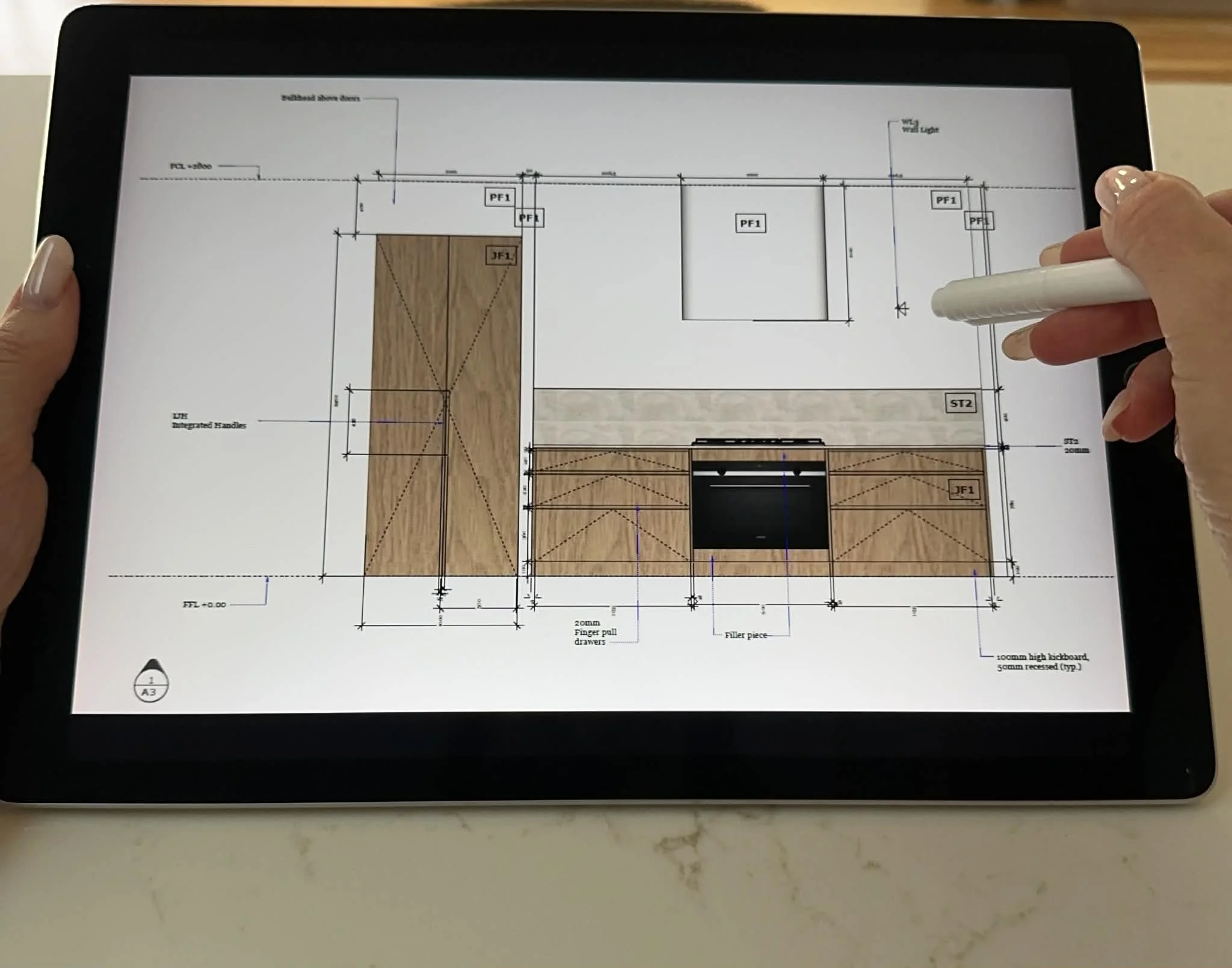 Floor plan drawing on a tablet, featuring wooden flooring, cabinets, and measurement details for a construction or renovation project.
