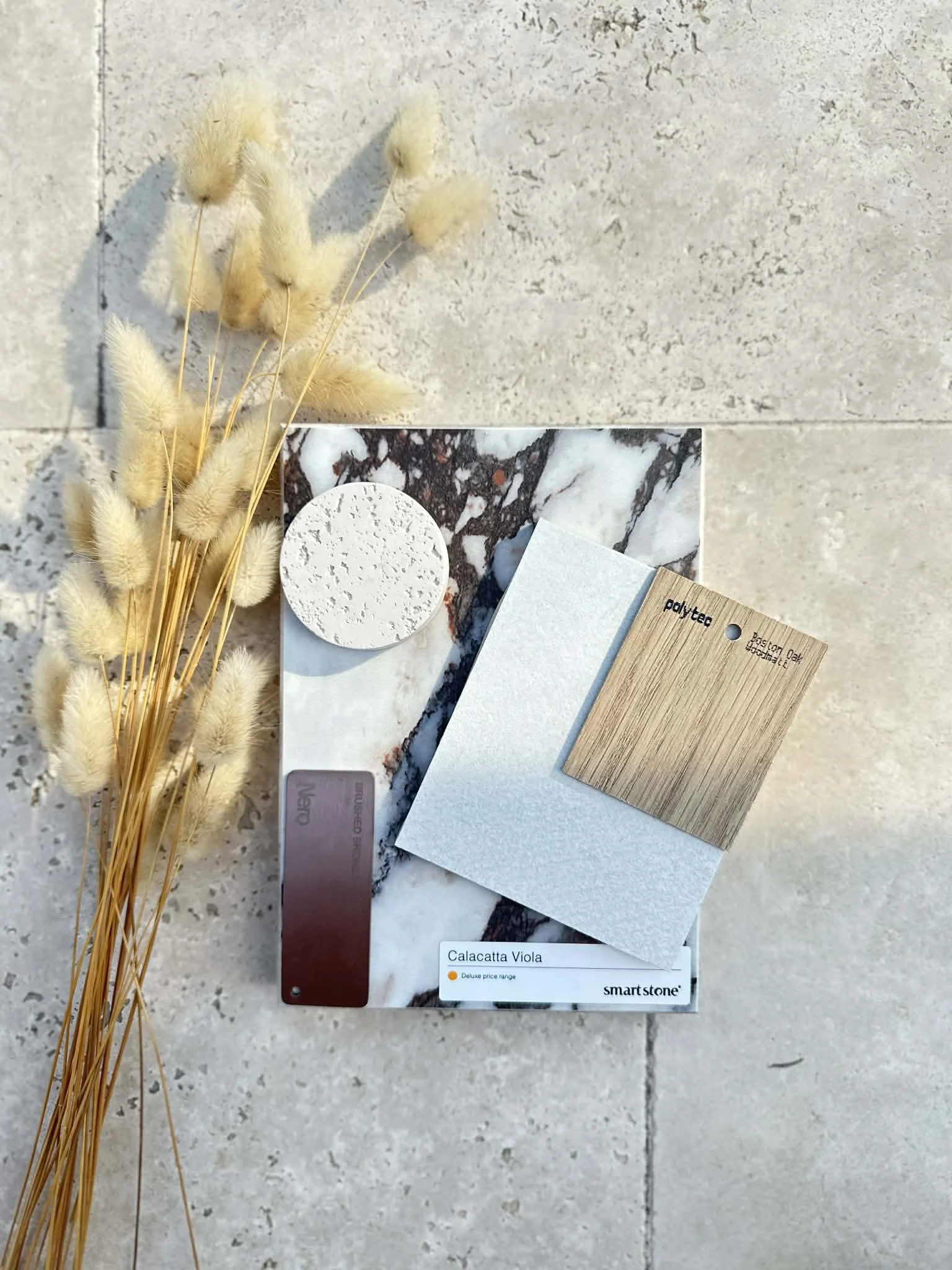 Various fabric and material samples, a bunch of dried beige grasses, and a color swatch labeled 'Calacatta Viola' on a tiled surface.