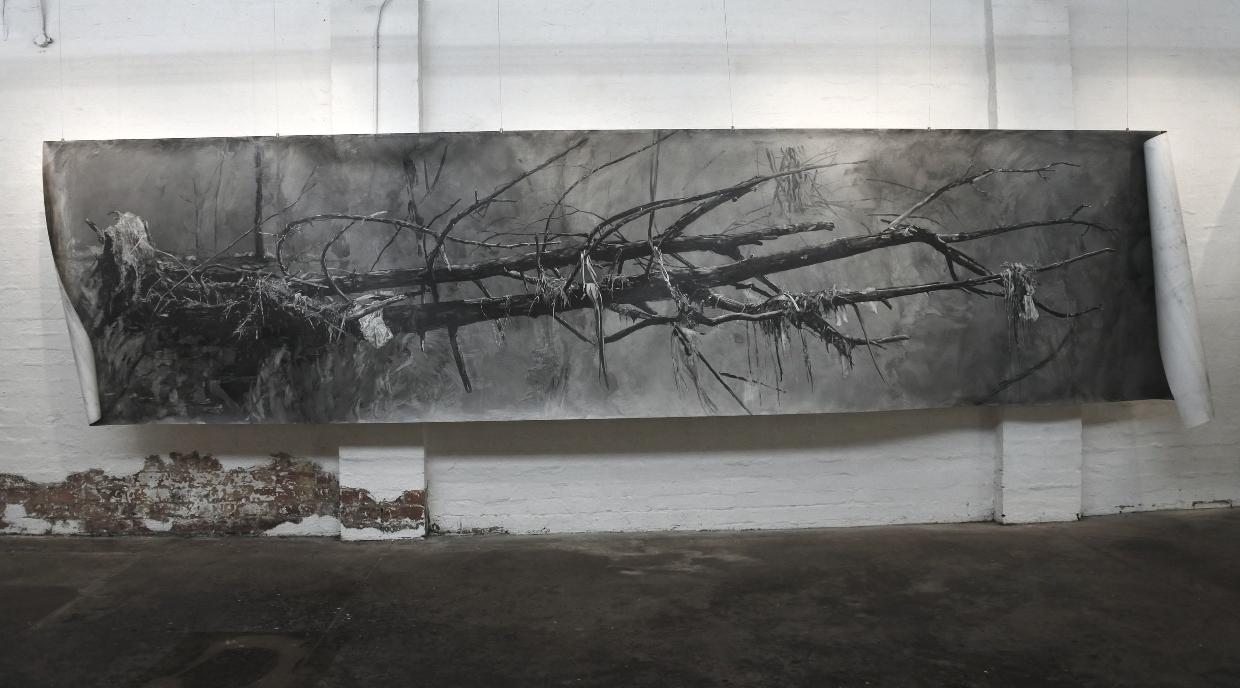 Black and white painting of a fallen tree with roots and branches, displayed on a white brick wall.