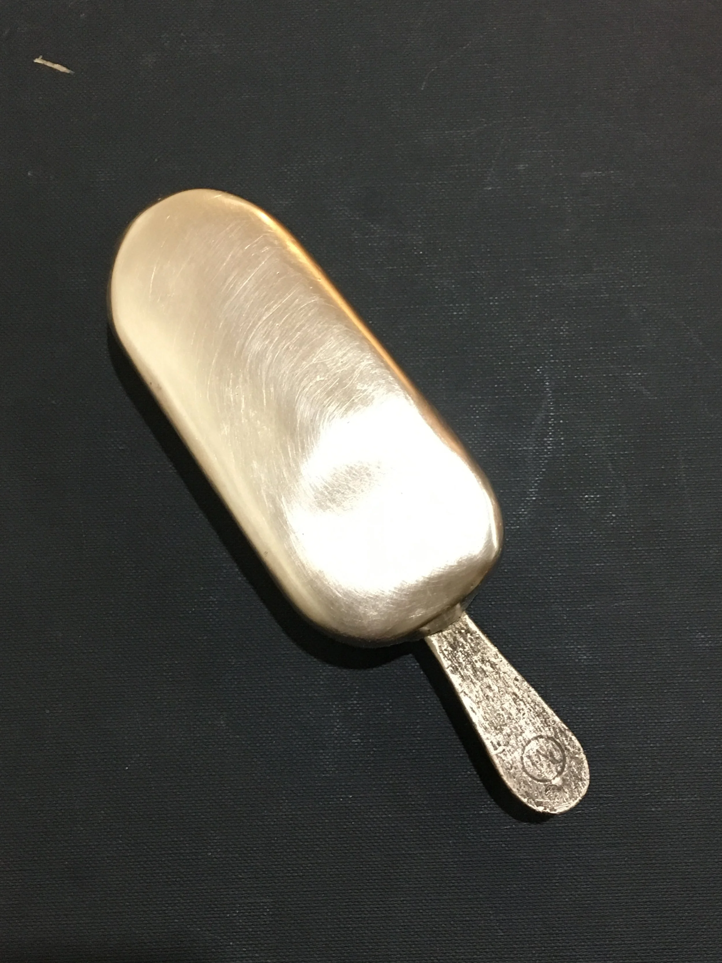 A bronze popsicle with a blunt end and a flat stick handle.