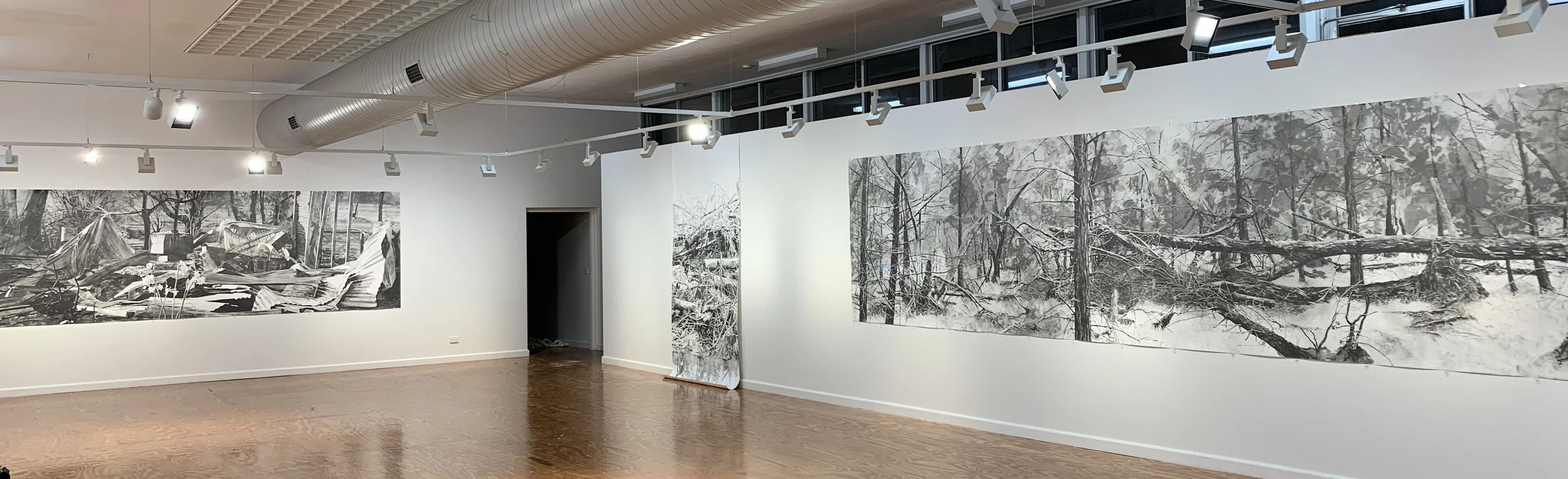 An art gallery with black and white landscape drawings, depicting post destructive events in various landscapes.