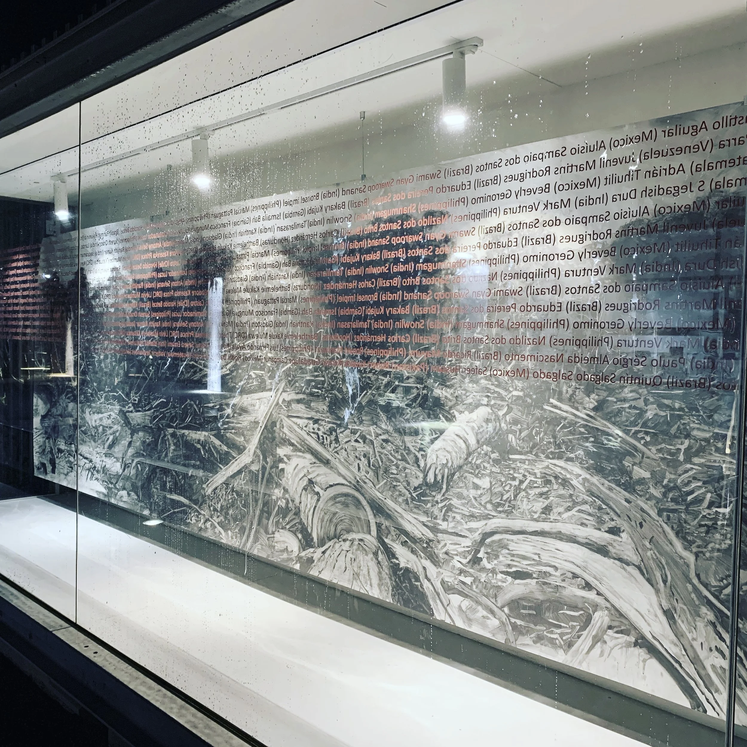 A reflection of a glass wall with red and black text in a store window, showing informational content. The wall appears wet with water droplets and streaks, and the reflection of interior lighting is visible.