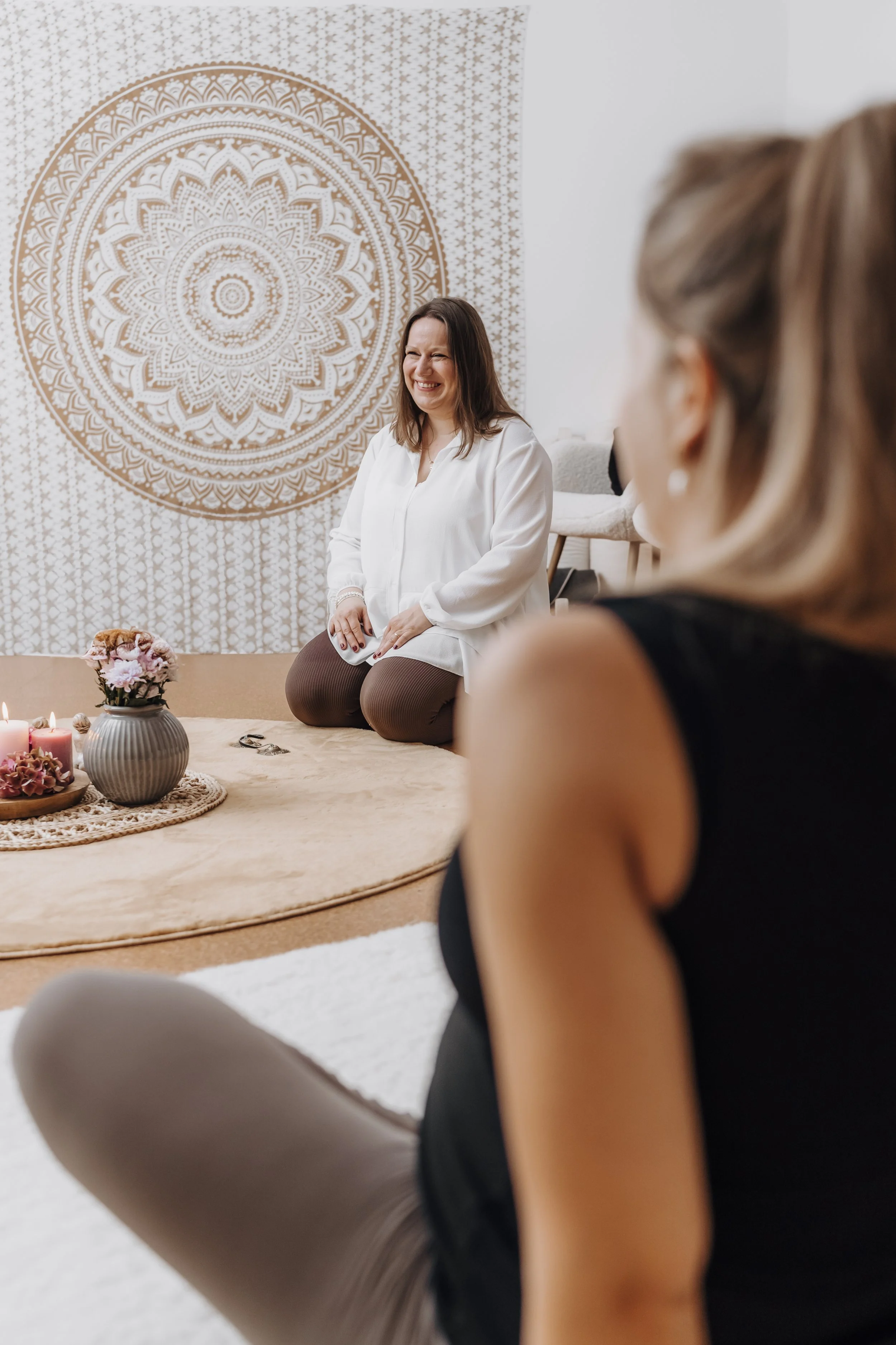 Geburtsvorbereiterin sitzt in einem Raum und lächelt ihre Teilnehmerin freundlich an