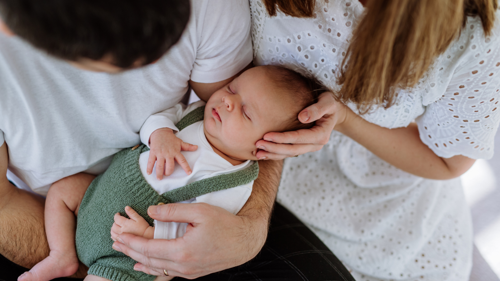 Ein Neugeborenes wird liebevoll von seiner Mutter und seinem Vater gehalten und getragen.