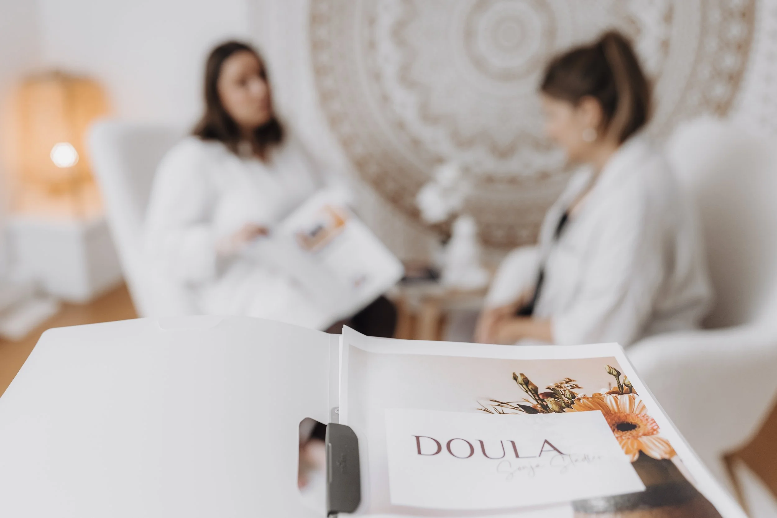 Ein Katalog auf einem Tisch trägt den Titel 'DOULA' und zeigt ein Blumenbild.