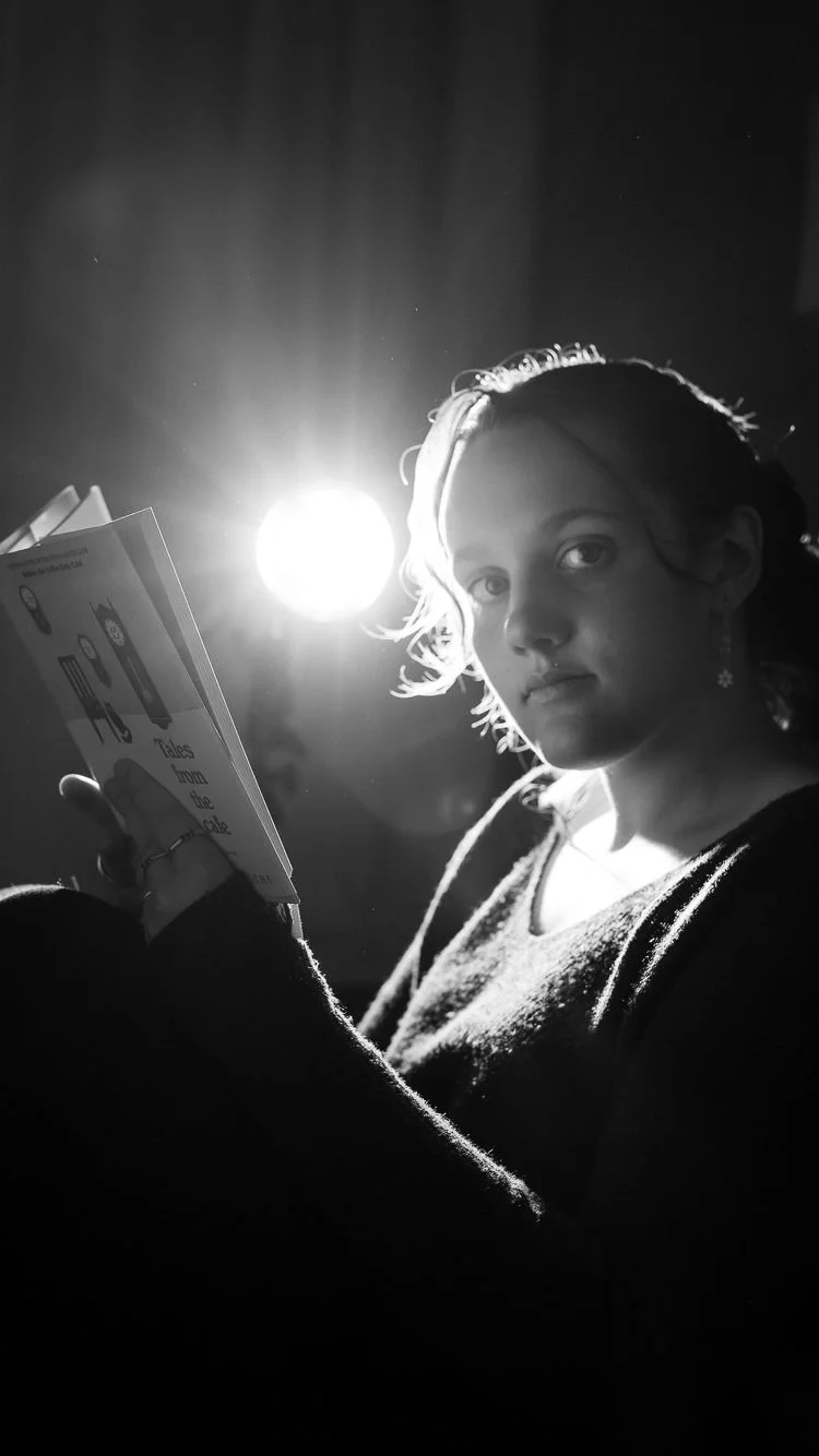 Black and white photo of a young woman reading a book, with bright light source behind her head creating a halo effect.