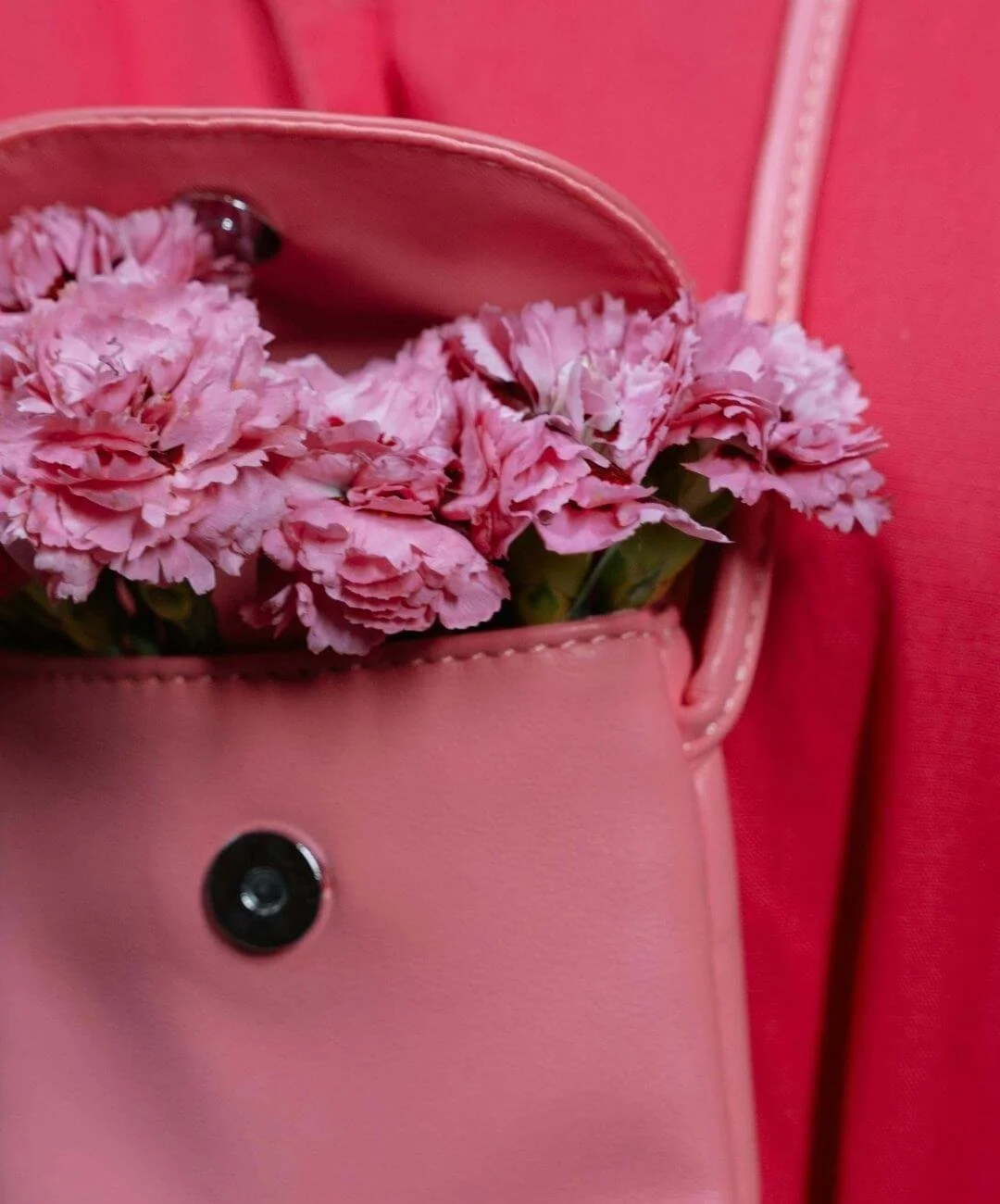Pink flowers in a pink handbag against a pink background.