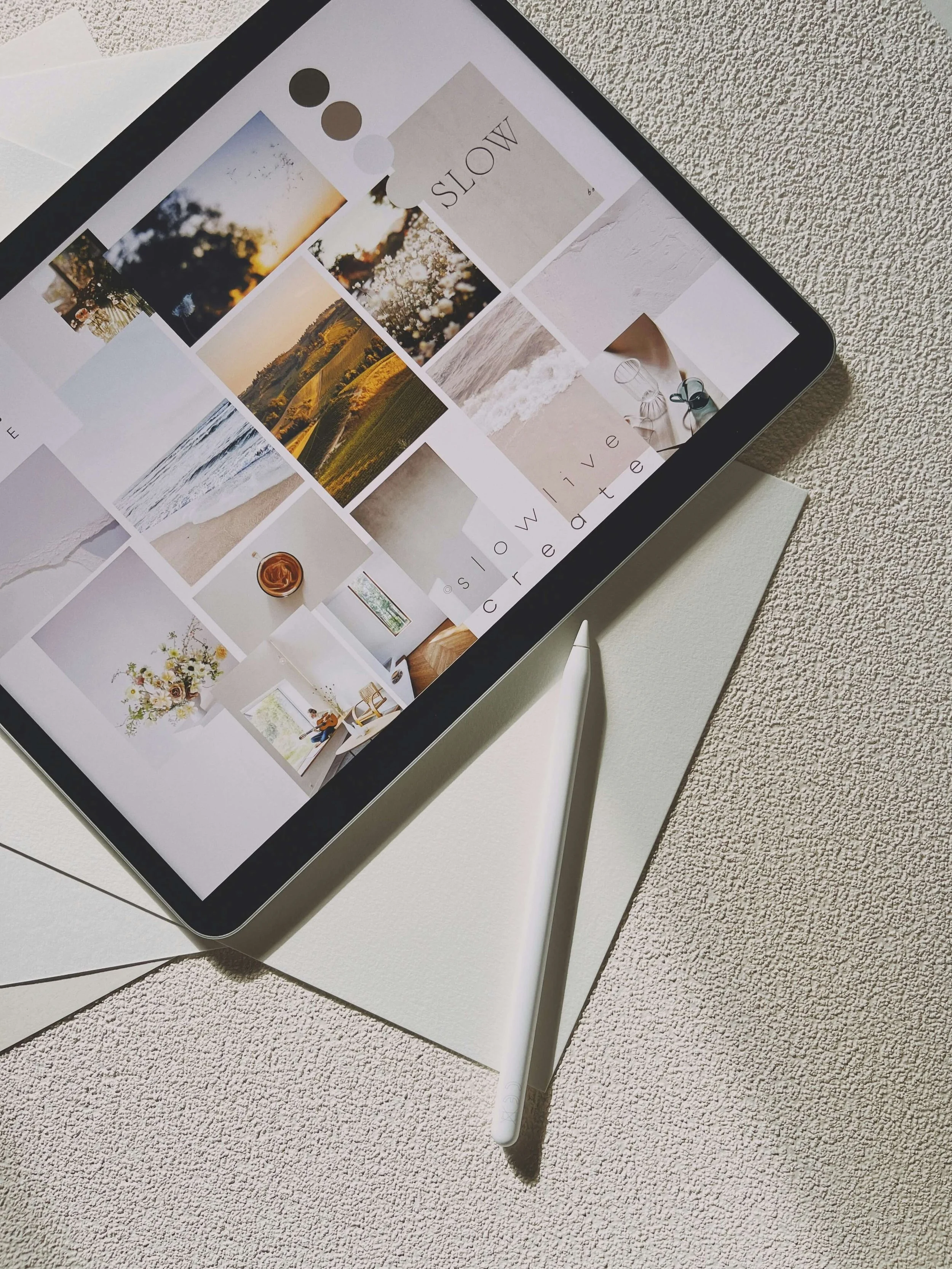 An iPad displaying a collage of photos, placed on a white textured surface with a white stylus pencil adjacent to it.