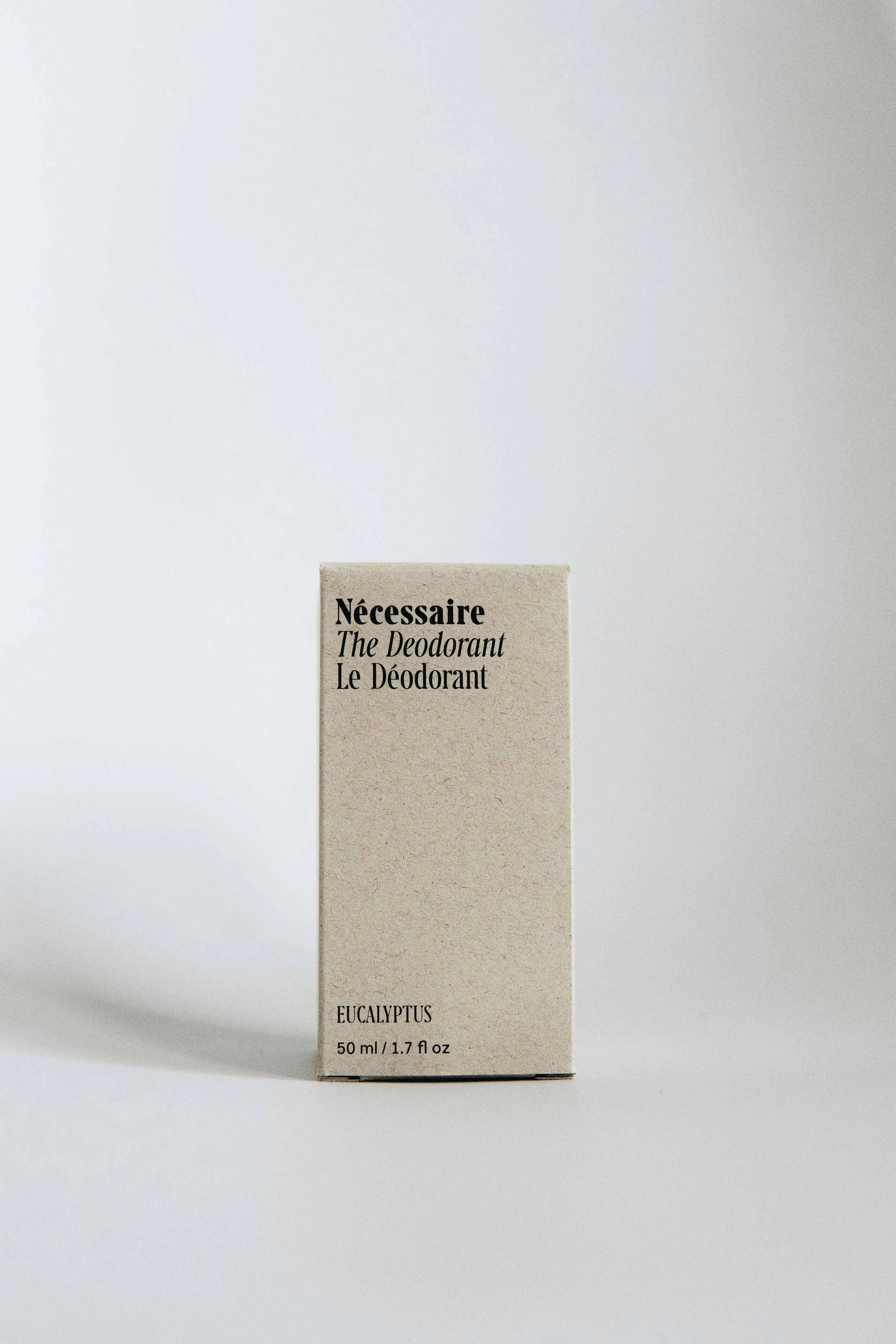 A beige box labeled "Nécessaire" with text "The Deodorant" and "Le Déodorant" in black, along with notes about eucalyptus scent and 50 ml/1.7 fl oz size, standing on a white surface against a plain background.