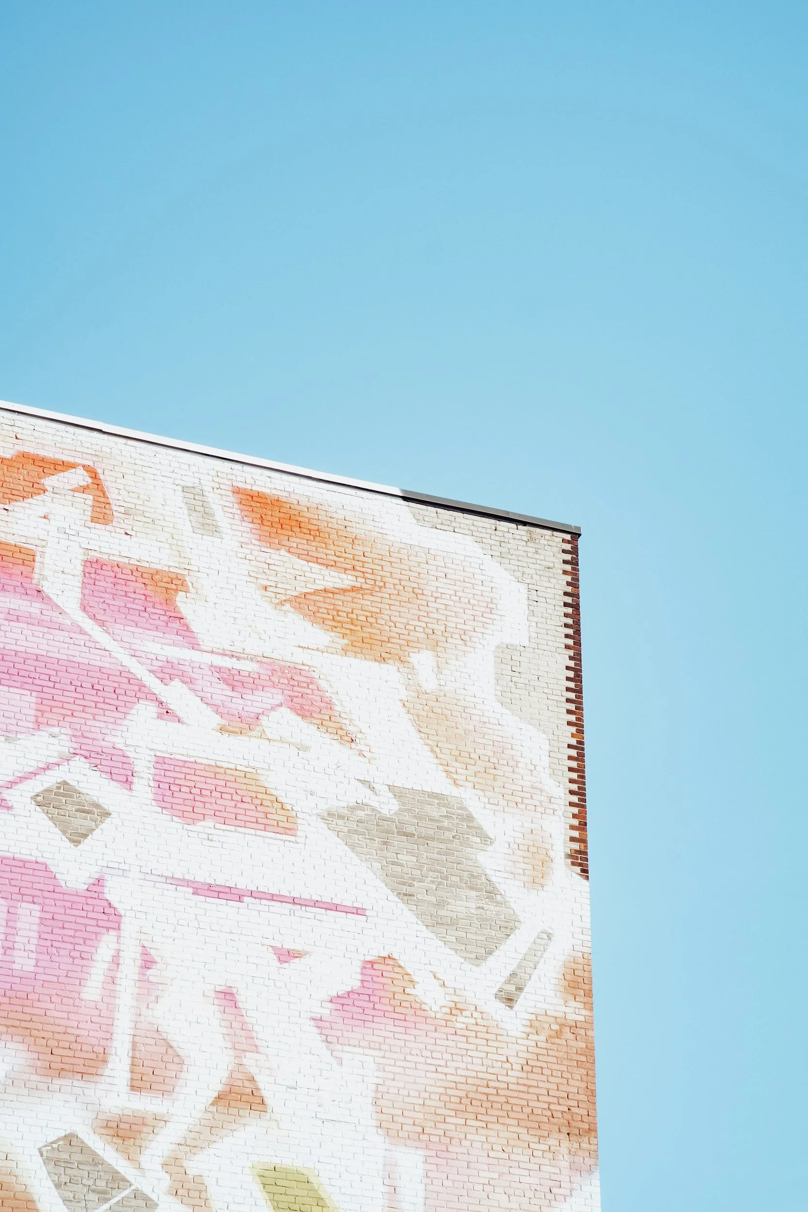 A partially visible mural painted on a brick building wall with soft pastel colors against a clear blue sky.
