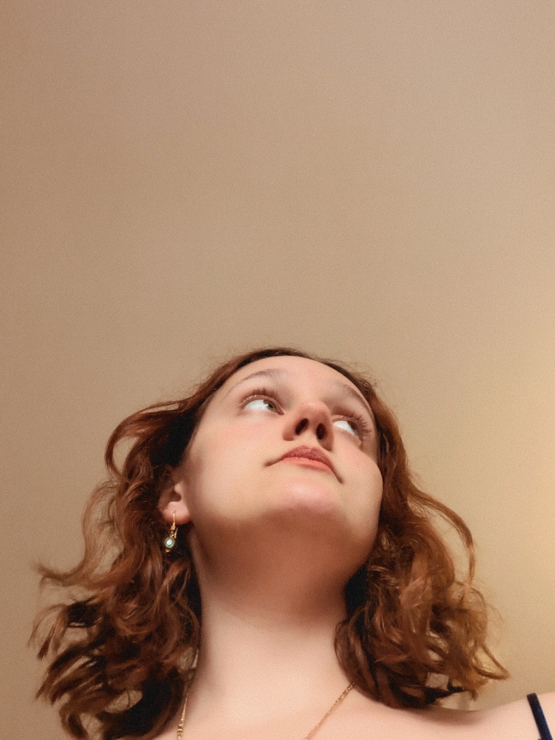 A young woman with curly red hair looking upwards with a beige ceiling in the background.
