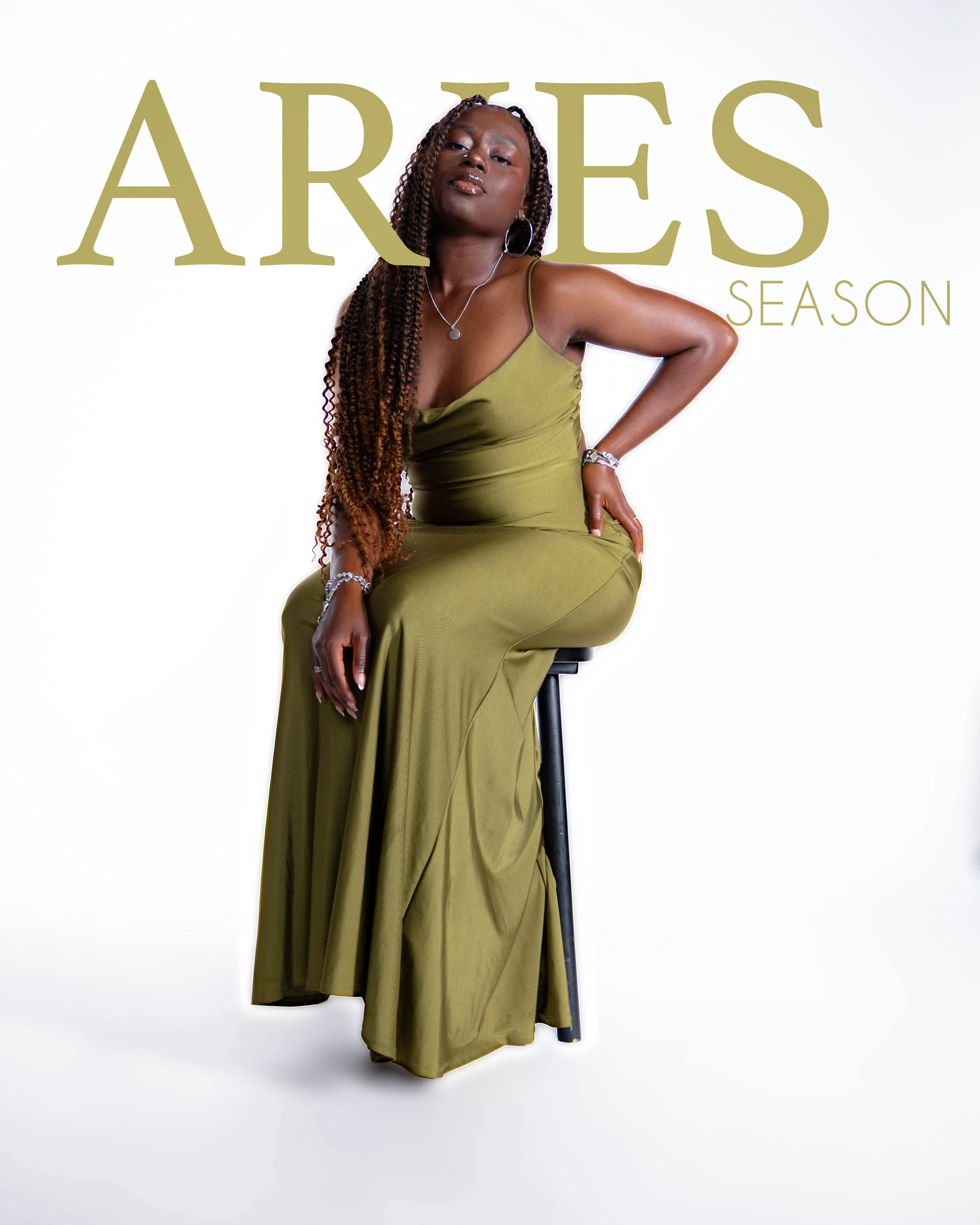 Woman with braided hair wearing an olive green dress, seated on a stool against a white background, with text reading 'ARIES SEASON' in large gold letters.