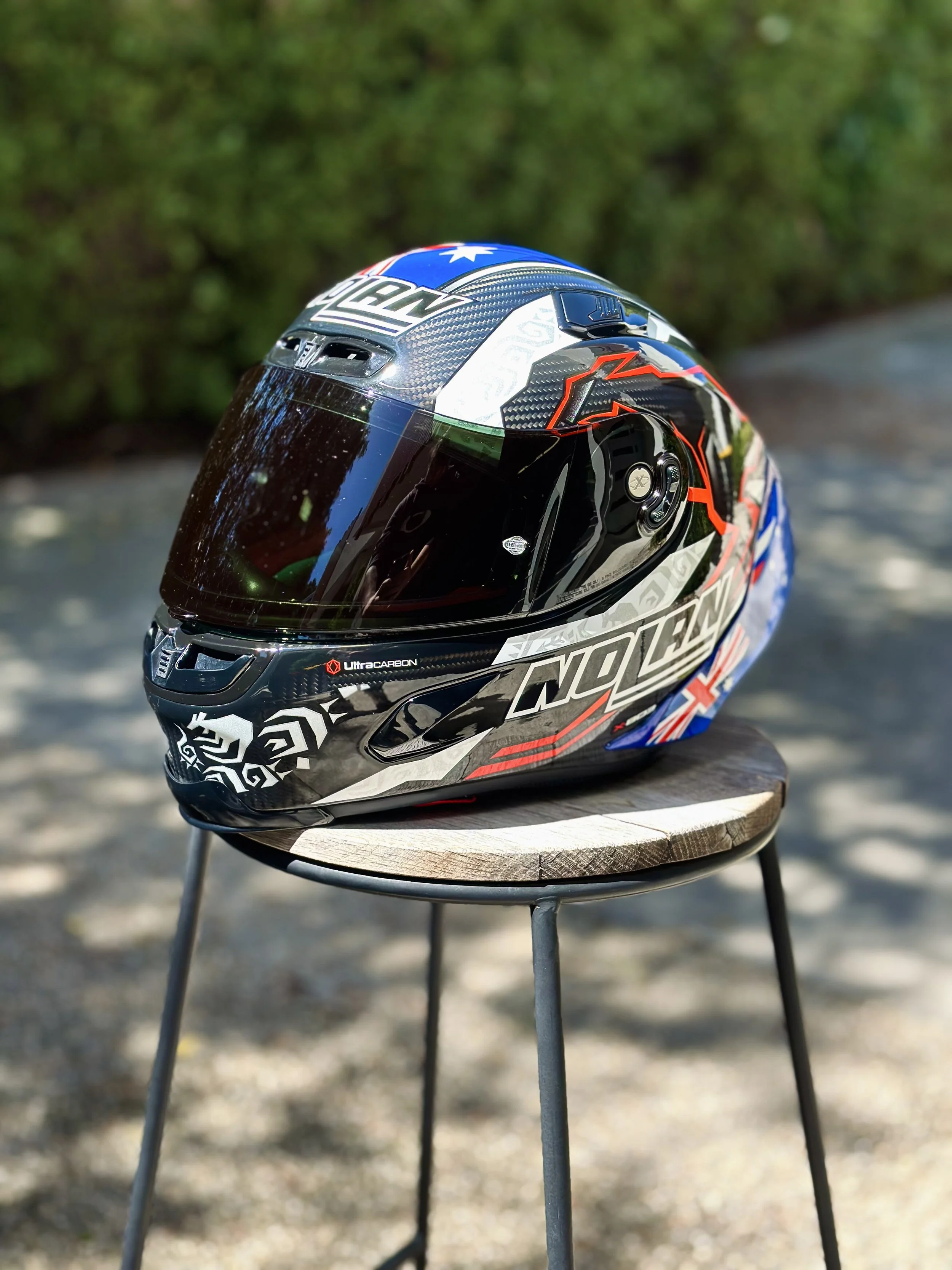A full-face motorcycle helmet with a black, white, red, and blue design placed on a wooden stool outdoors.