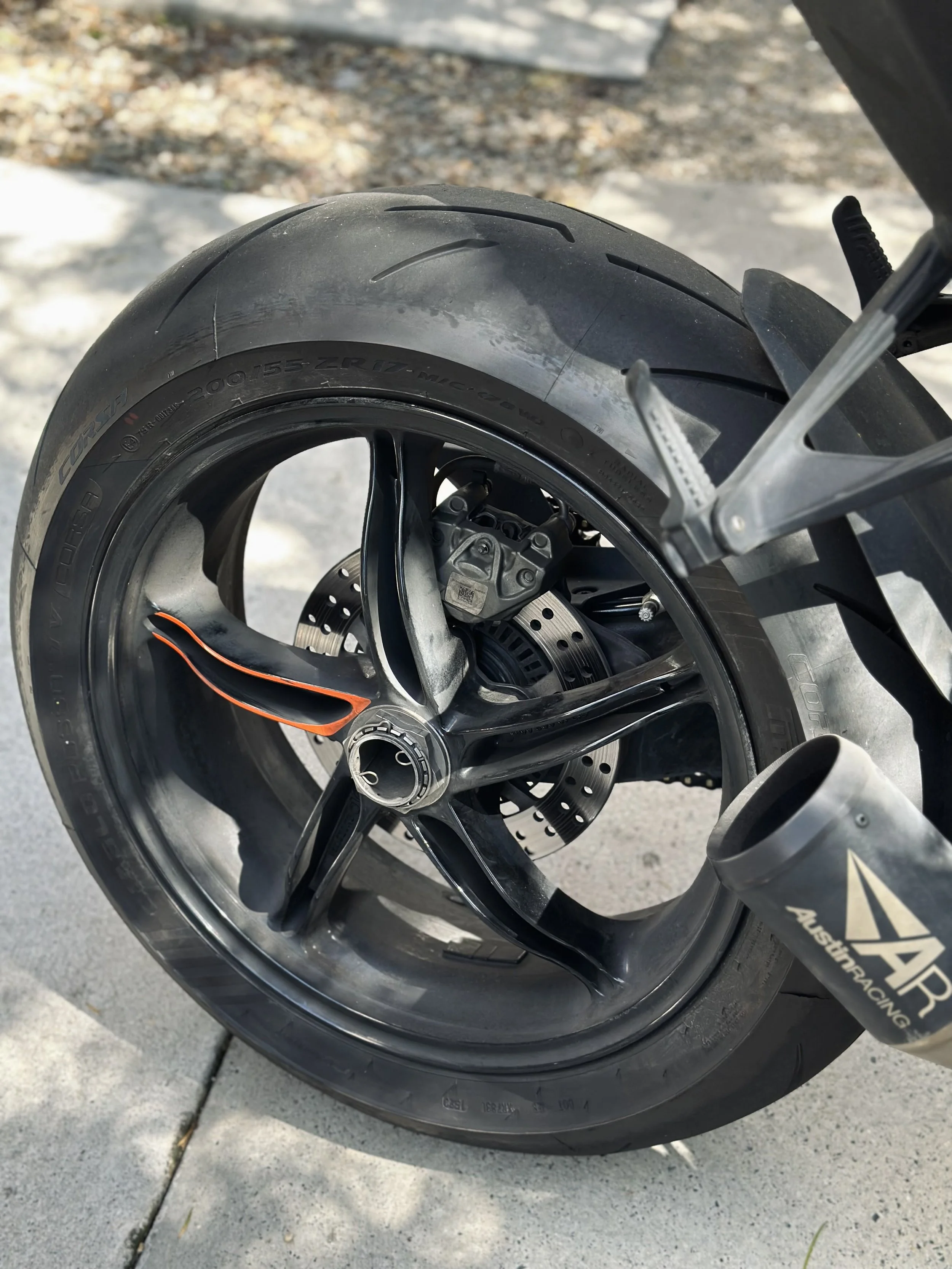 Close-up of a motorcycle rear wheel with a disc brake and a tire, showing details of the rim and tire treads.