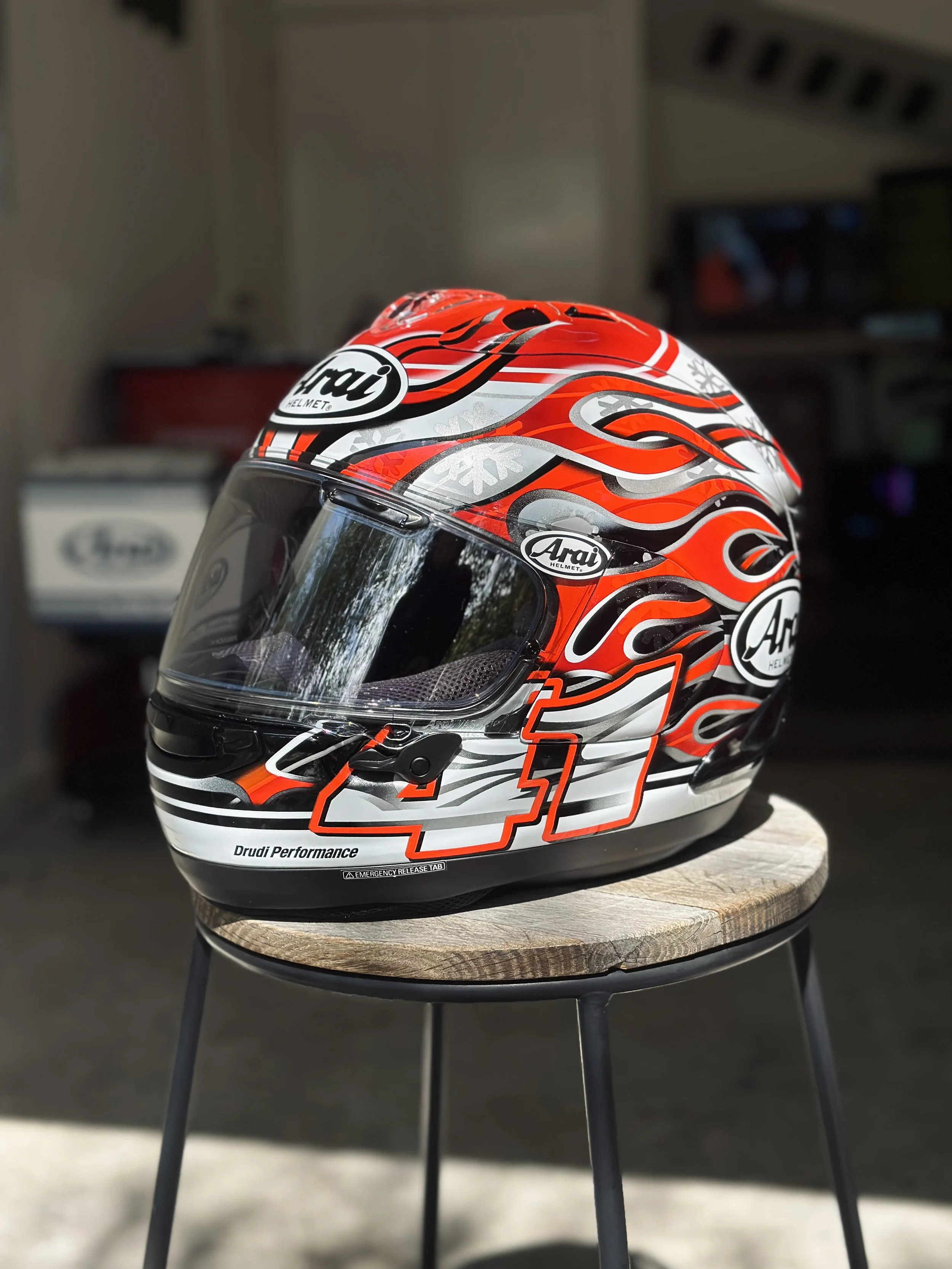 Motorcycle helmet with red, black, white, and silver fiery design, placed on a small round wooden and metal table.