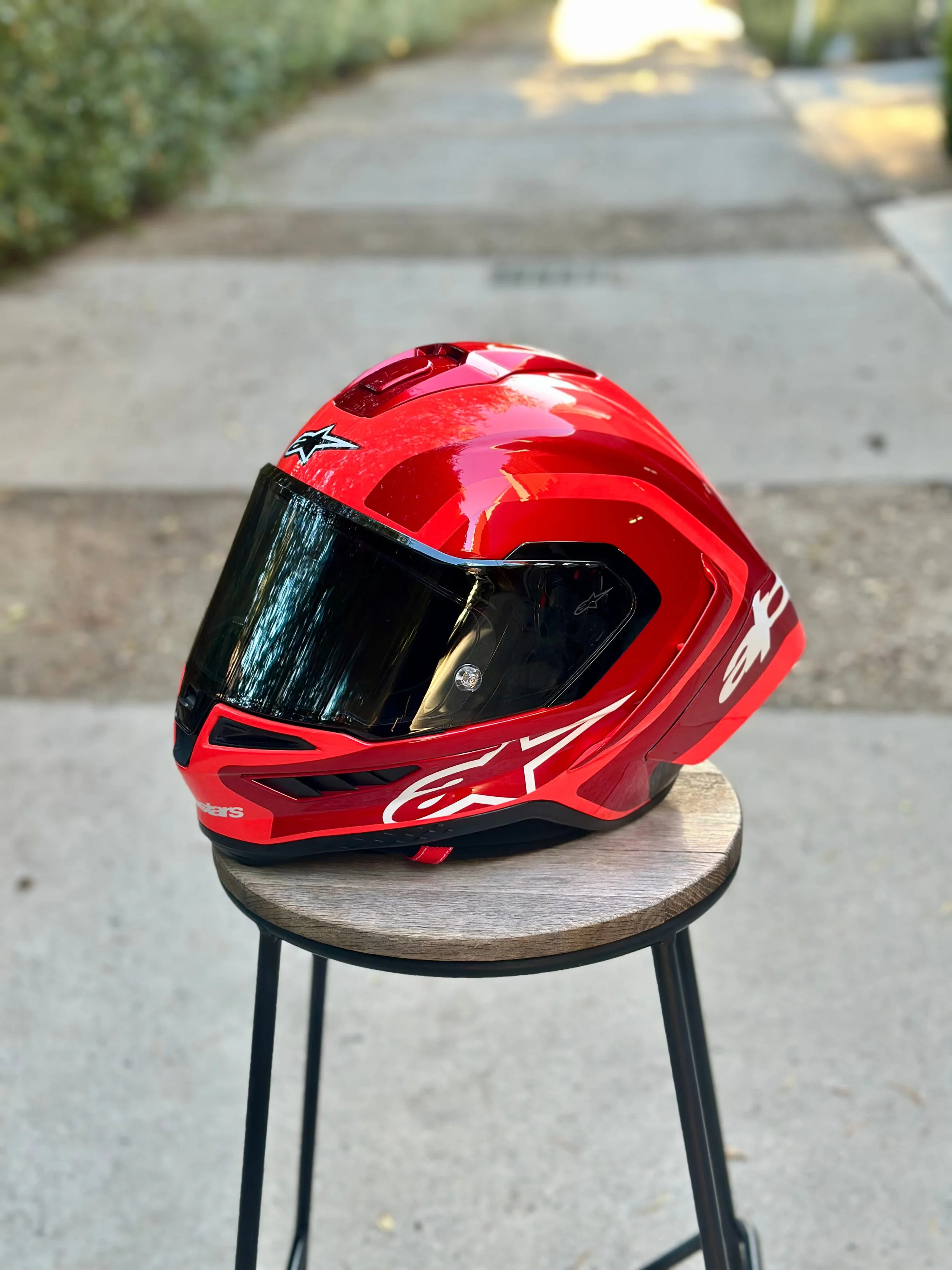 A red motorcycle helmet with a dark visor placed on a round wooden table outdoors.