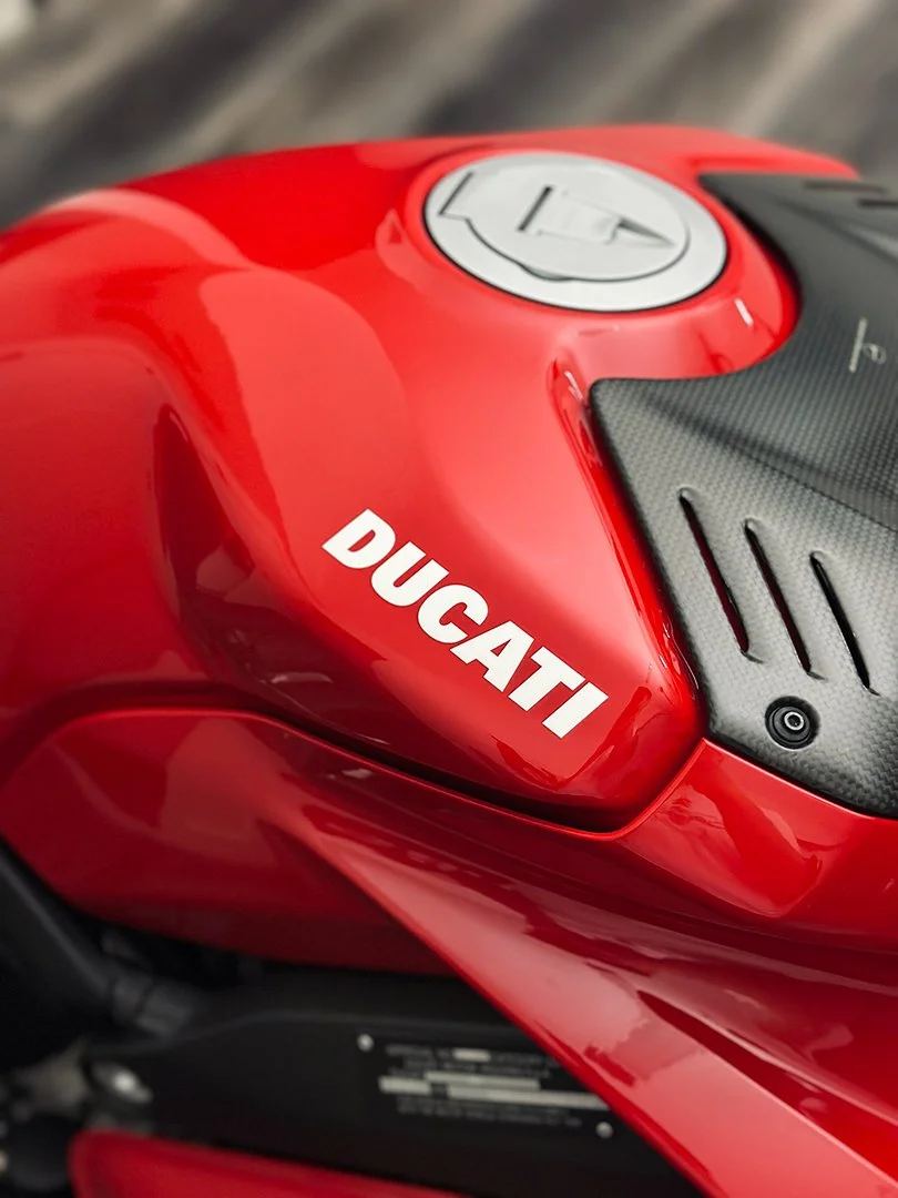 Close-up of a red Ducati motorcycle gas tank with a white Ducati logo and a black textured area.