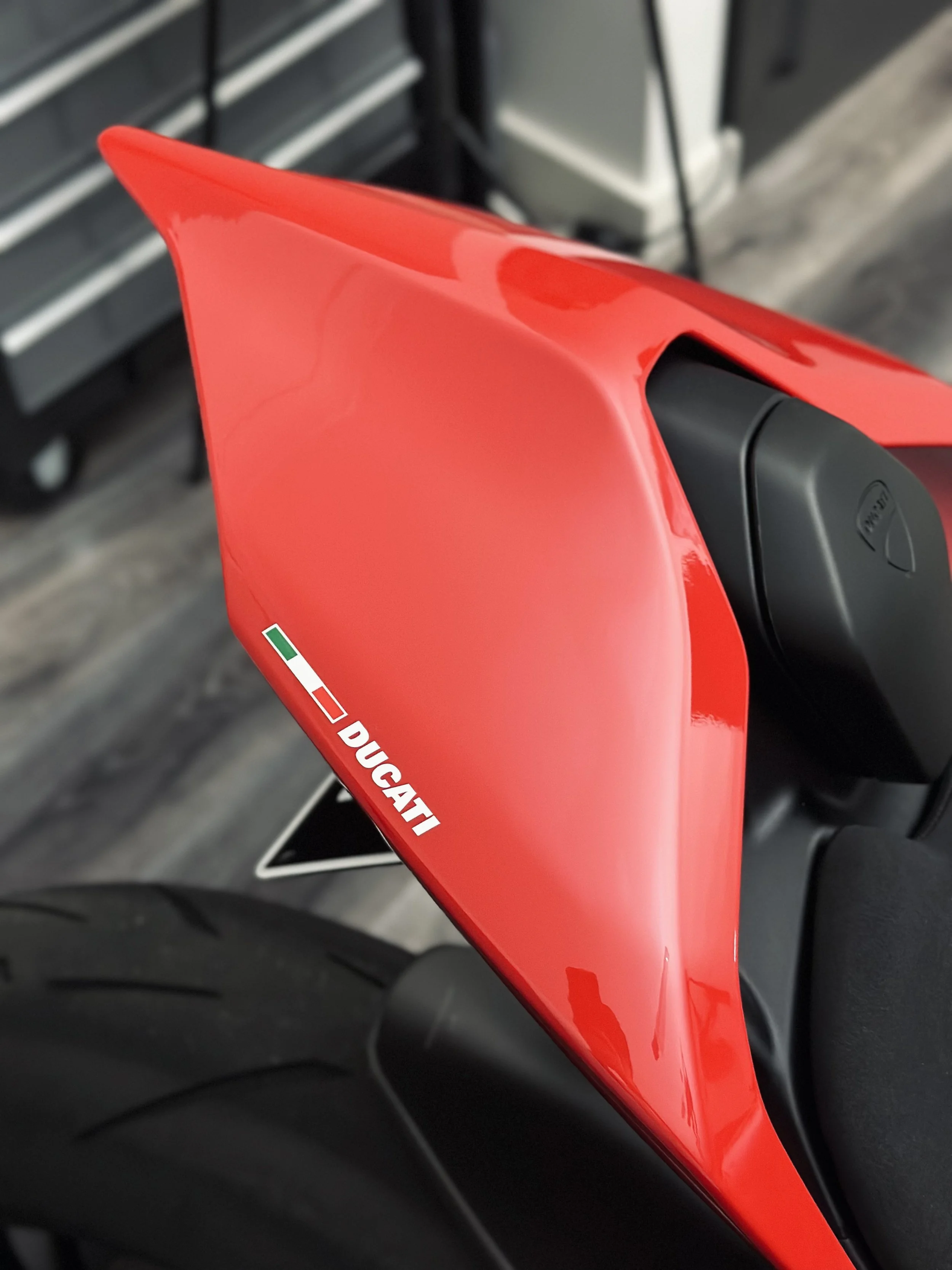 Close-up of a red Ducati motorcycle fuel tank with a black cap, showing the Ducati logo and a small Italian flag sticker.